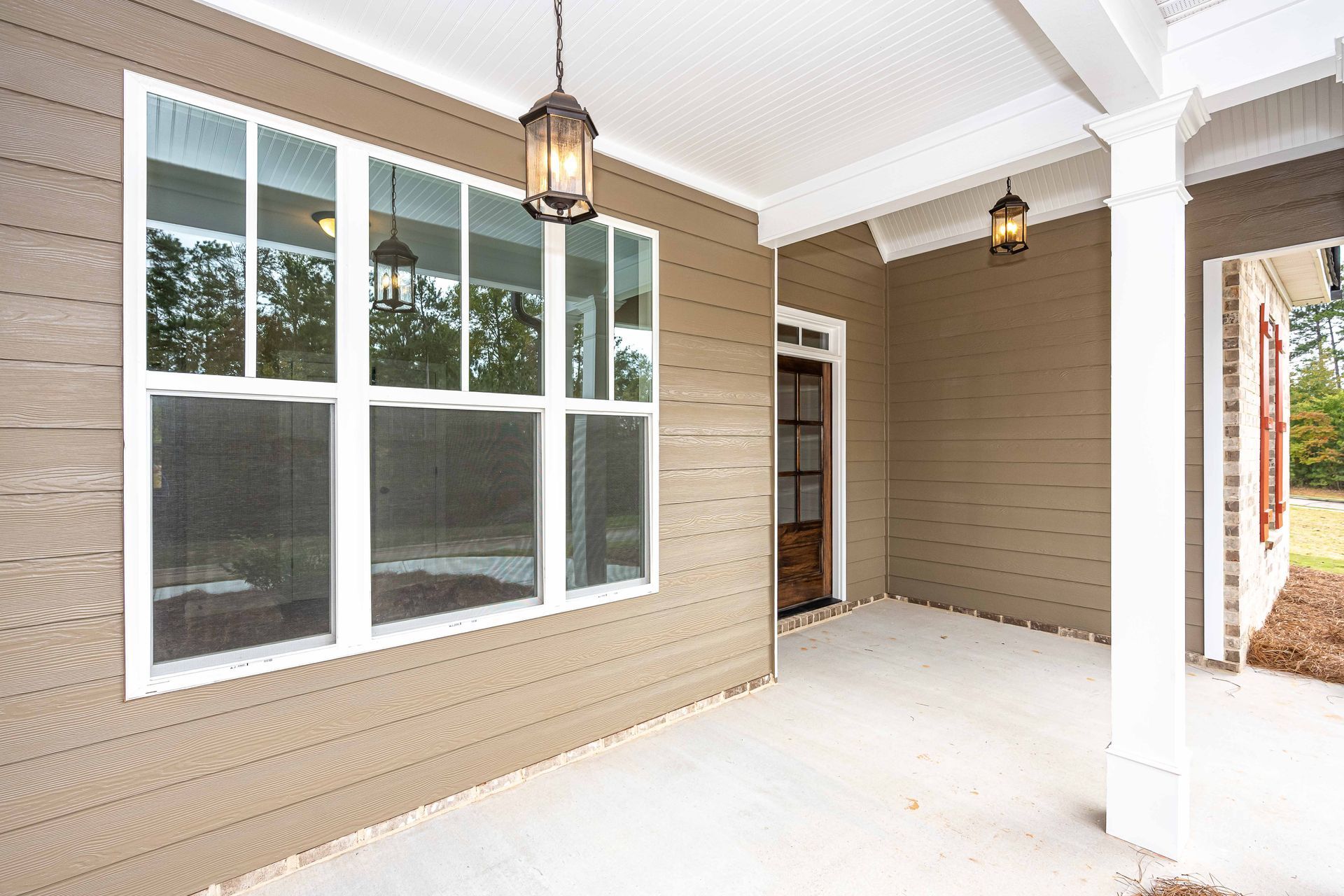 Covered front porch with beige siding, white columns, large window, and hanging lanterns.