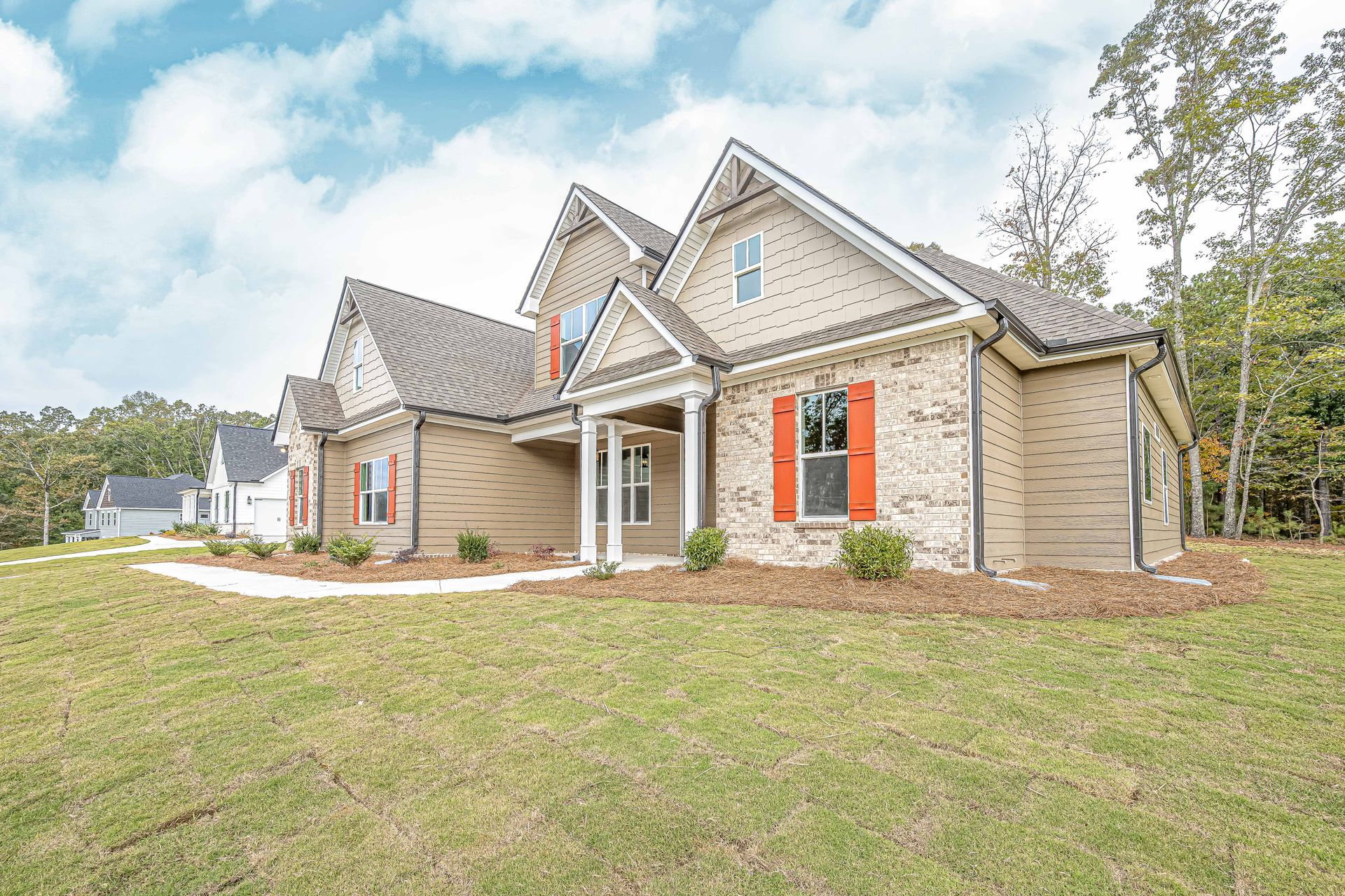Brick house with red shutters and a front lawn under a cloudy sky
