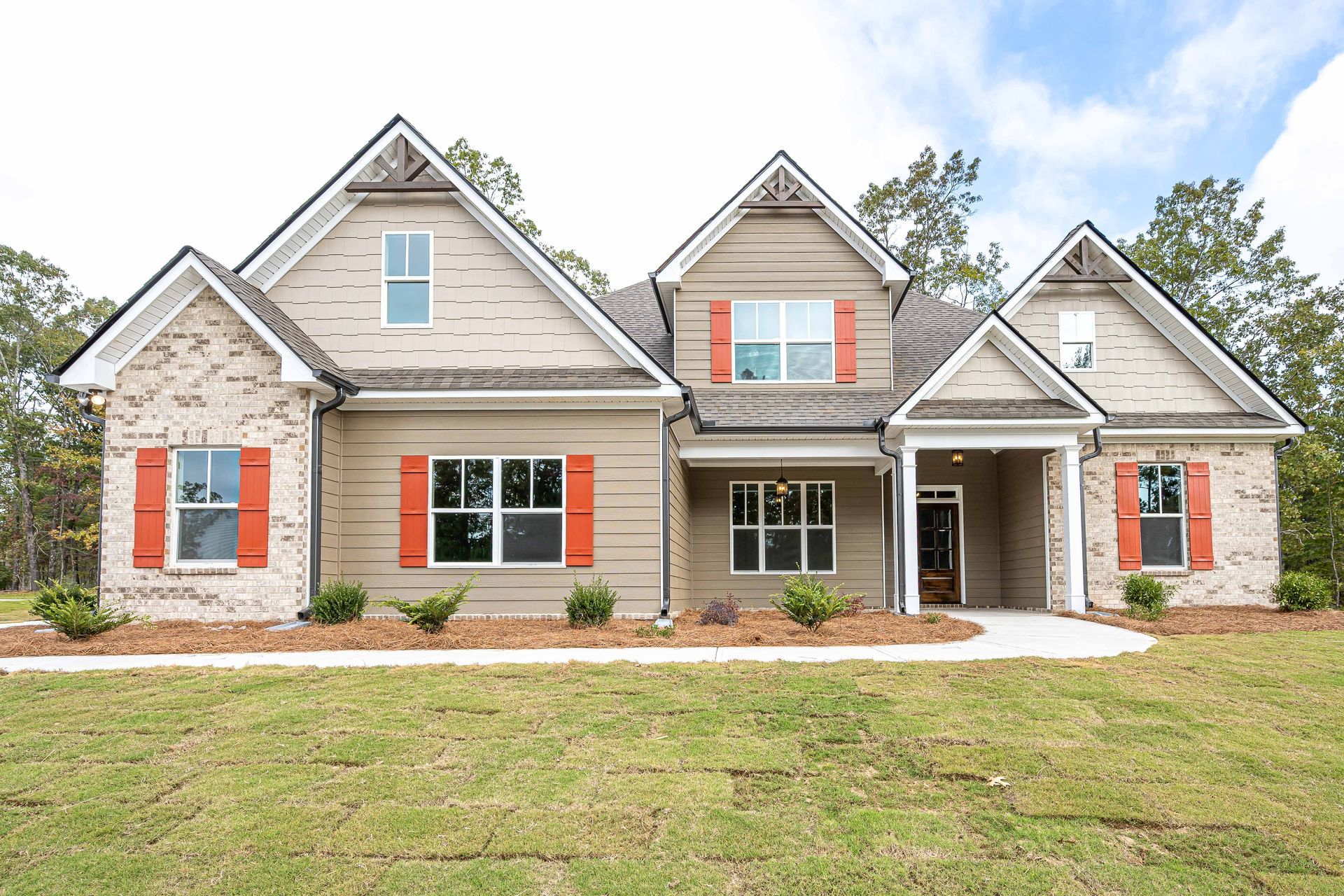 Front view of a gray stone suburban house with red shutters and a manicured lawn