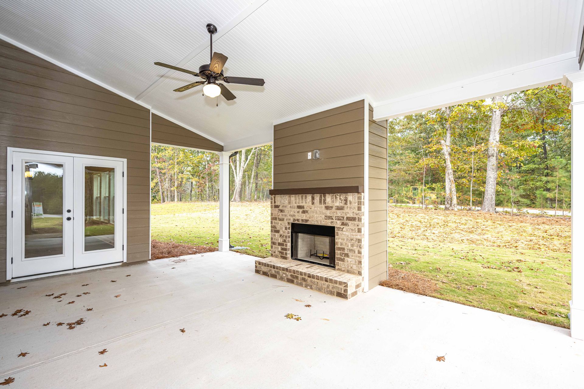 Covered patio with ceiling fan, brick fireplace, and open view of a grassy yard and trees