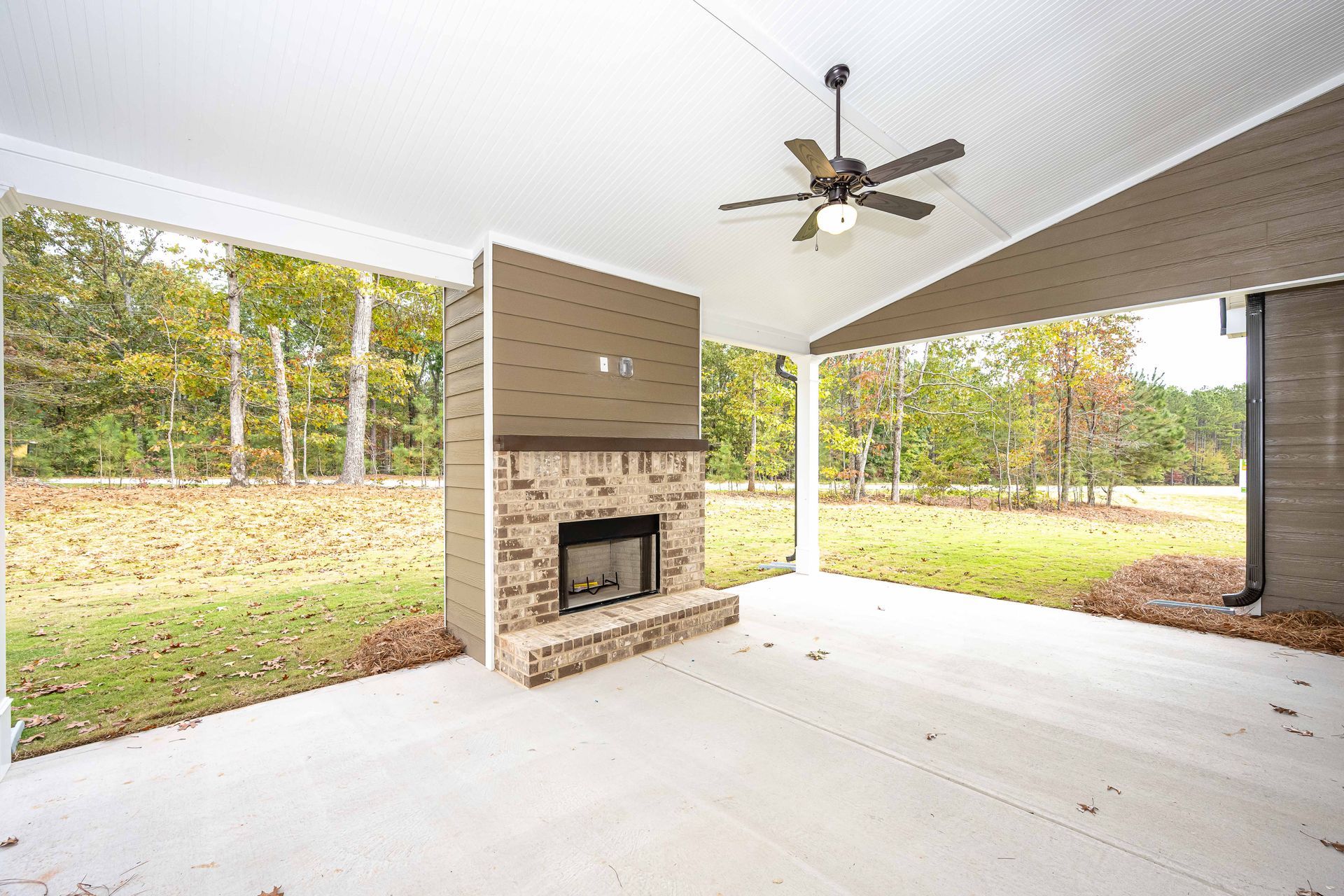 Covered patio with a stone fireplace, ceiling fan, and open view of a grassy yard.