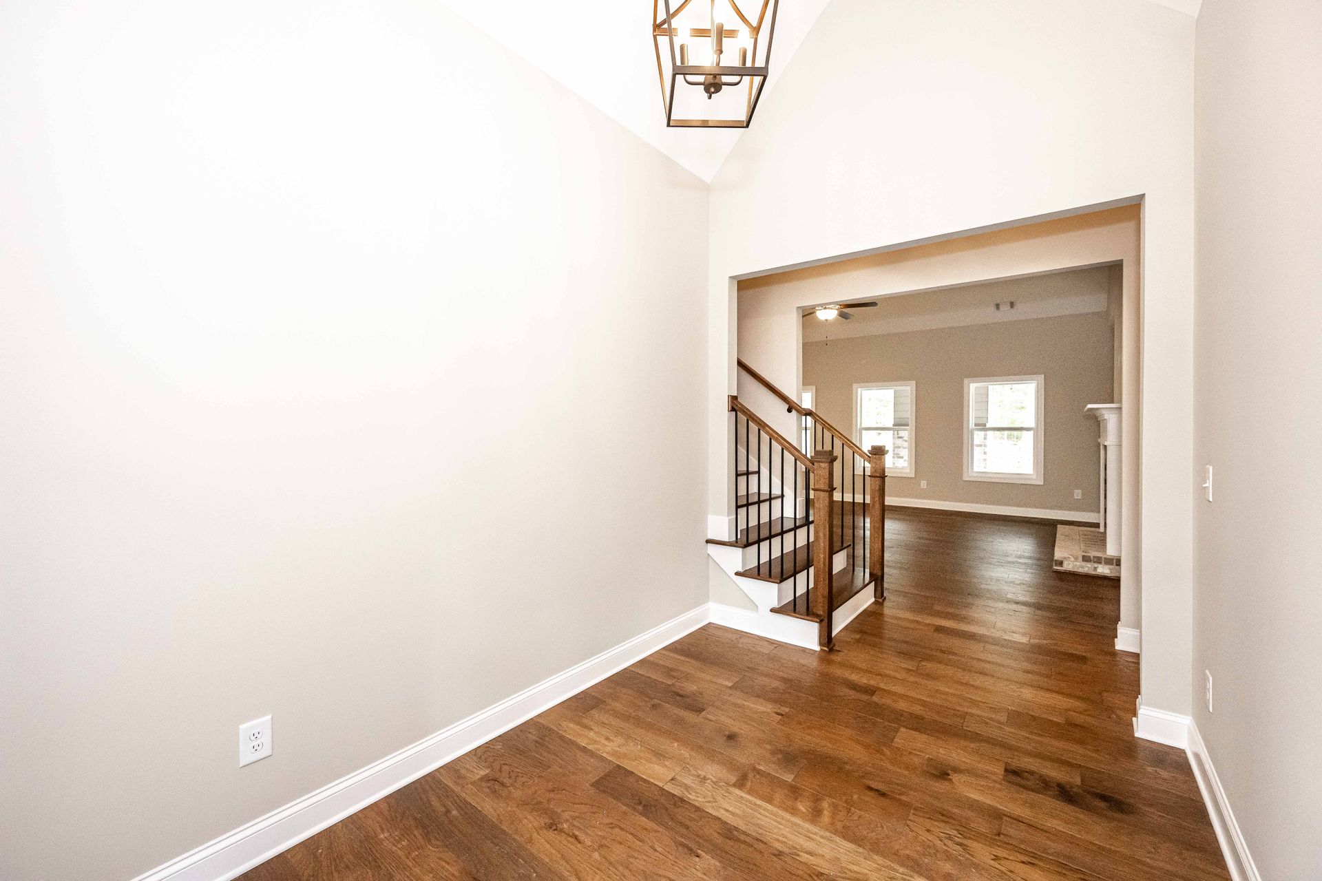 Empty entryway with hardwood floors, white walls, and a staircase visible through a wide opening.