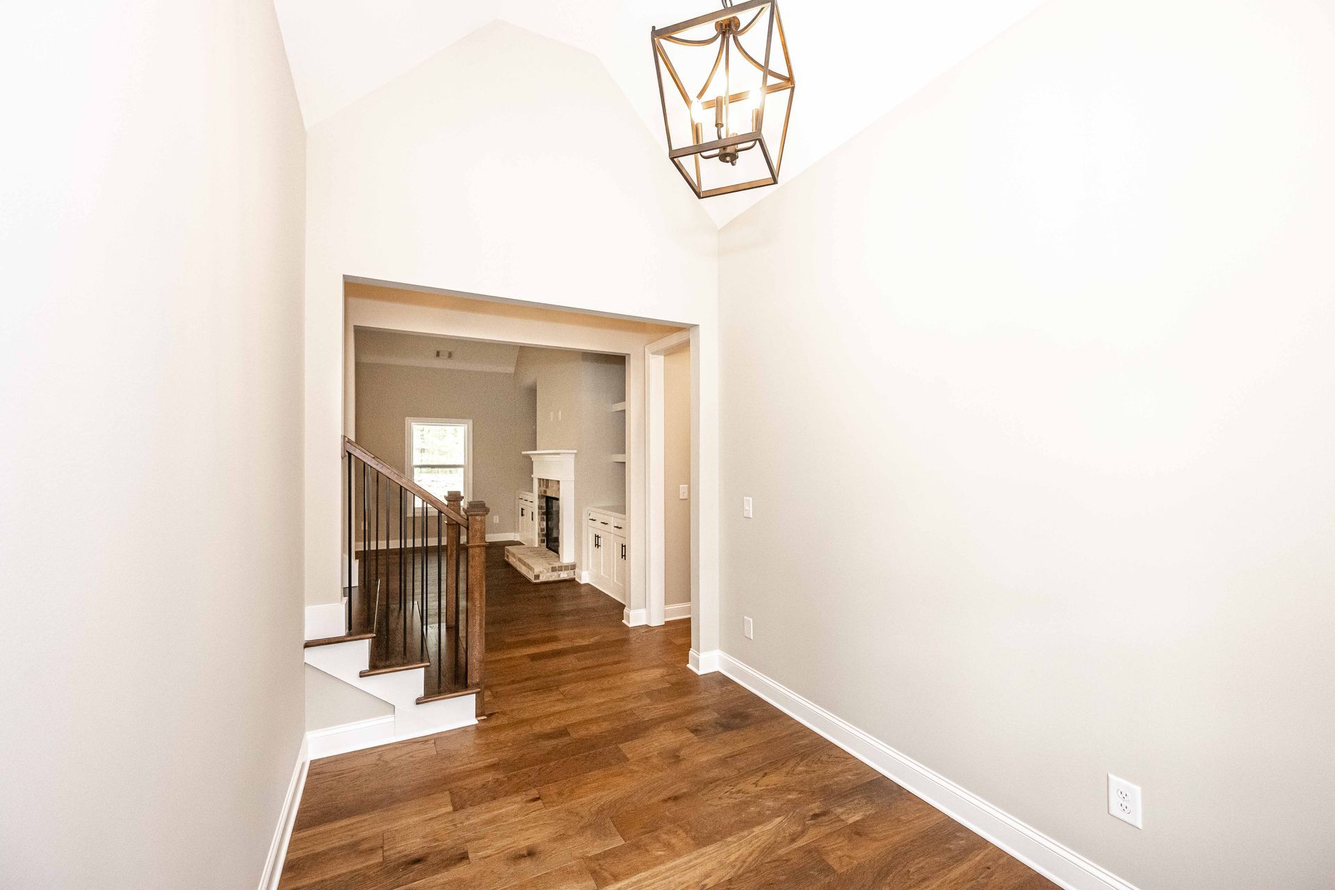 Empty hallway with hardwood floors, white walls, and a staircase visible through an open doorway