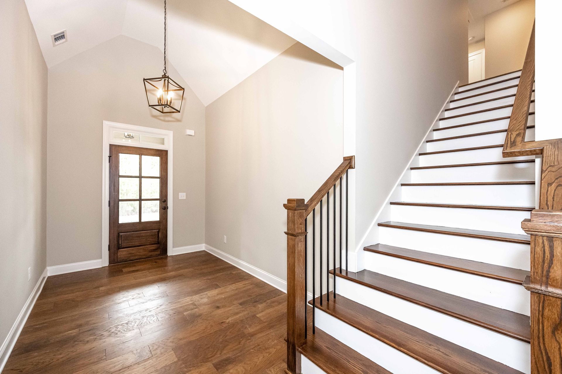 Bright foyer with wood floors, white walls, front door, and staircase with wooden railing