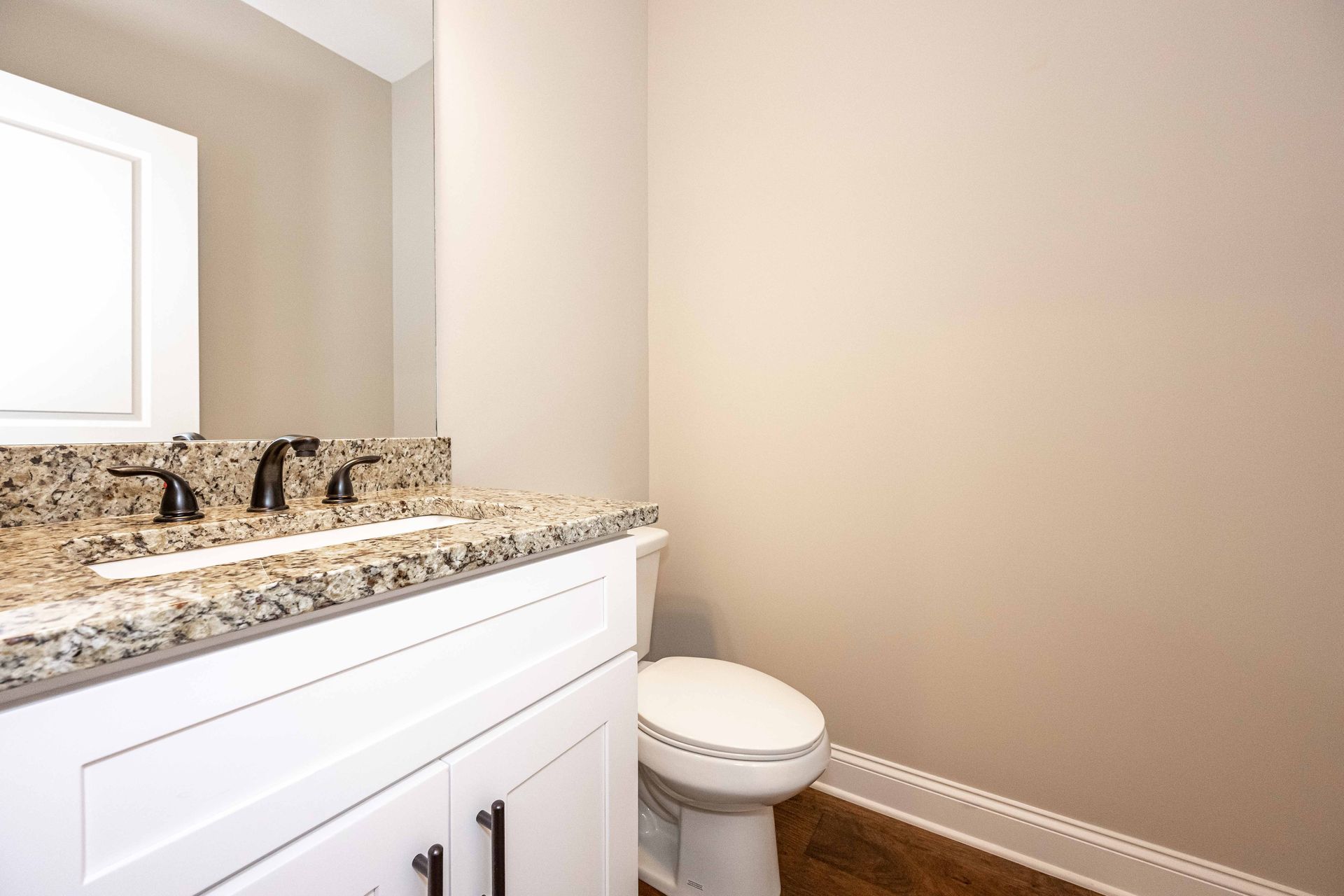 Small bathroom with white vanity, speckled granite countertop, toilet, and beige walls.