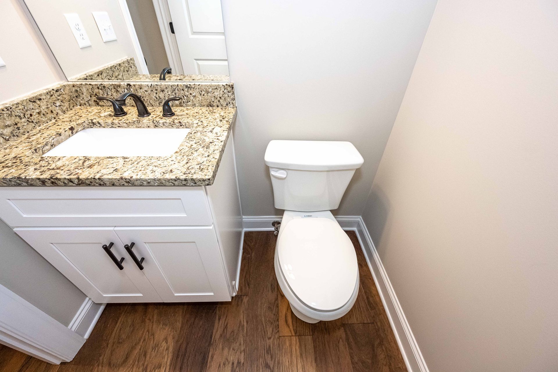 Small bathroom with white toilet, granite sink vanity, and wood-look floor.