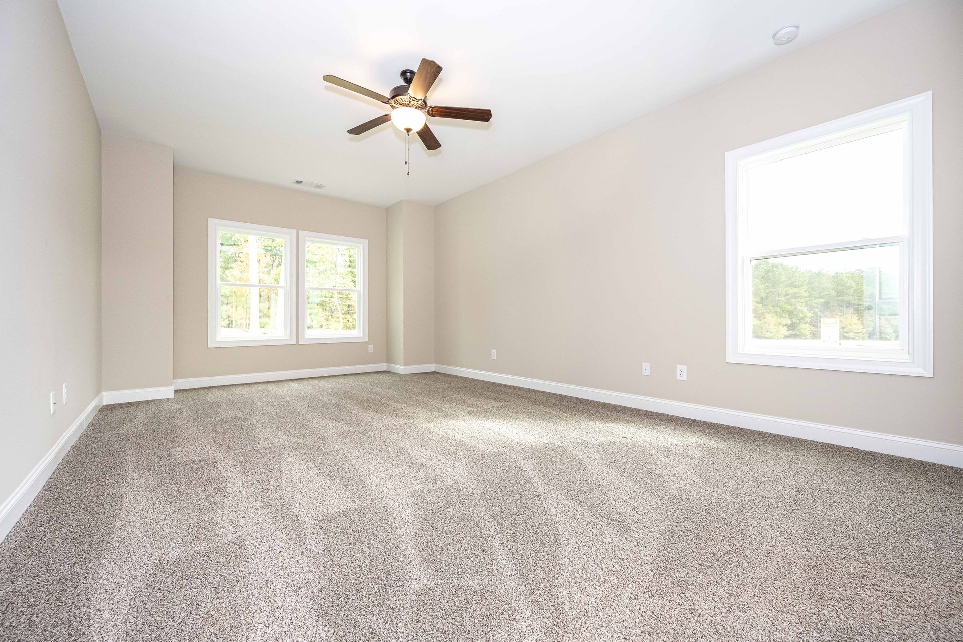 Empty beige carpeted living room with ceiling fan and two windows with blinds
