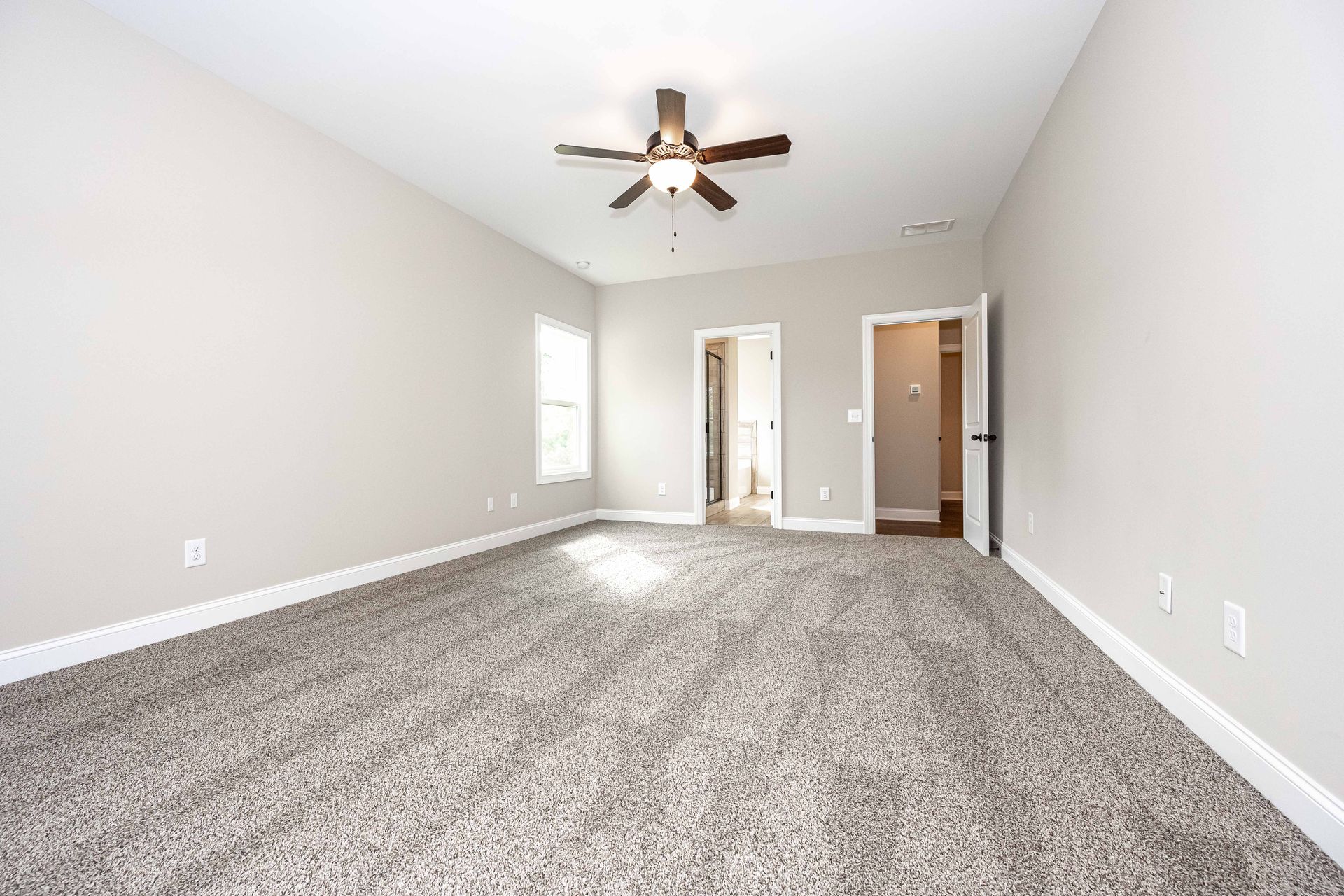 Empty carpeted living room with vaulted ceiling, ceiling fan, and doorway to hallway and entryway.