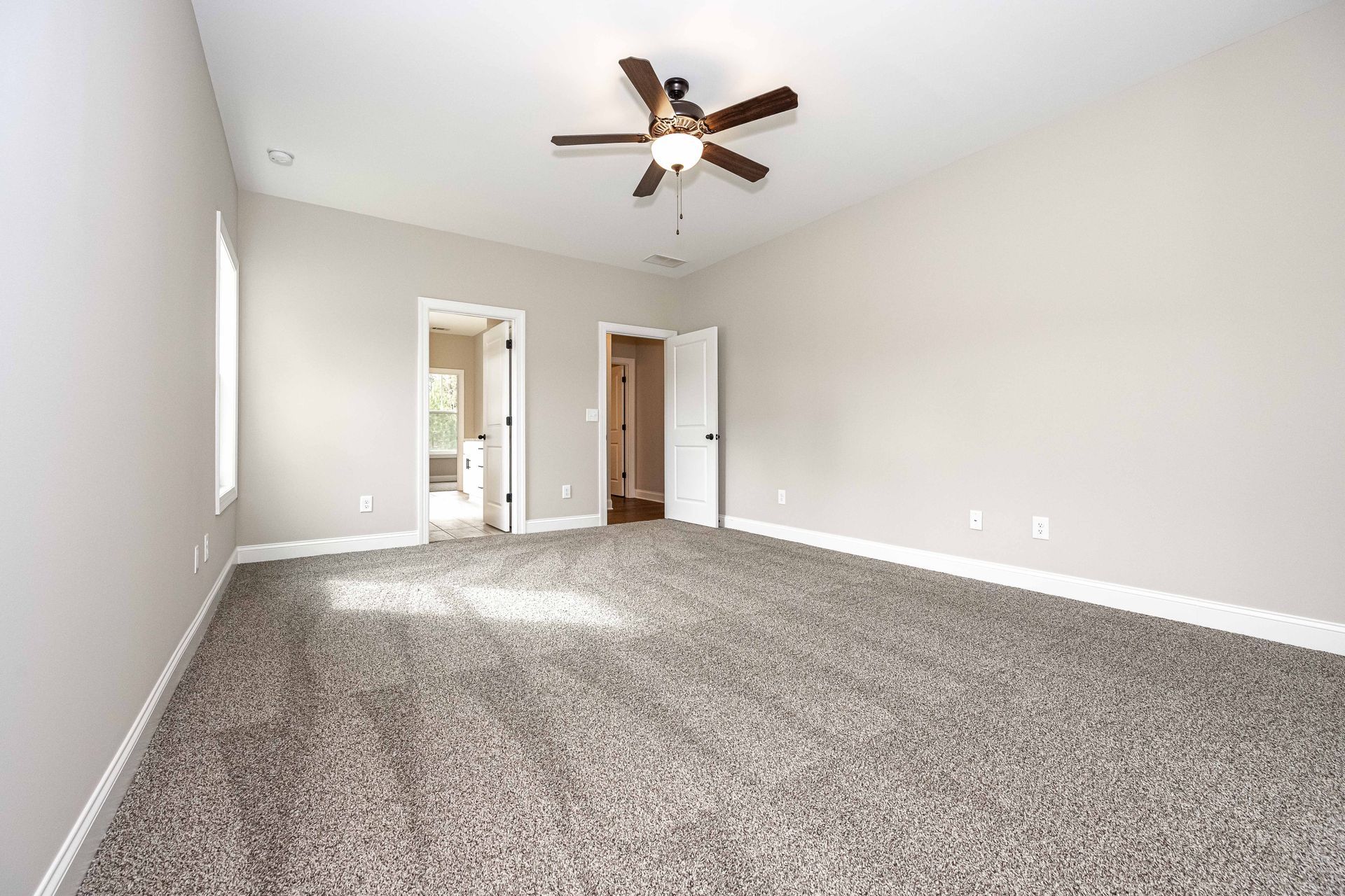 Empty carpeted bedroom with vaulted ceiling, ceiling fan, and open doorway to a hallway.