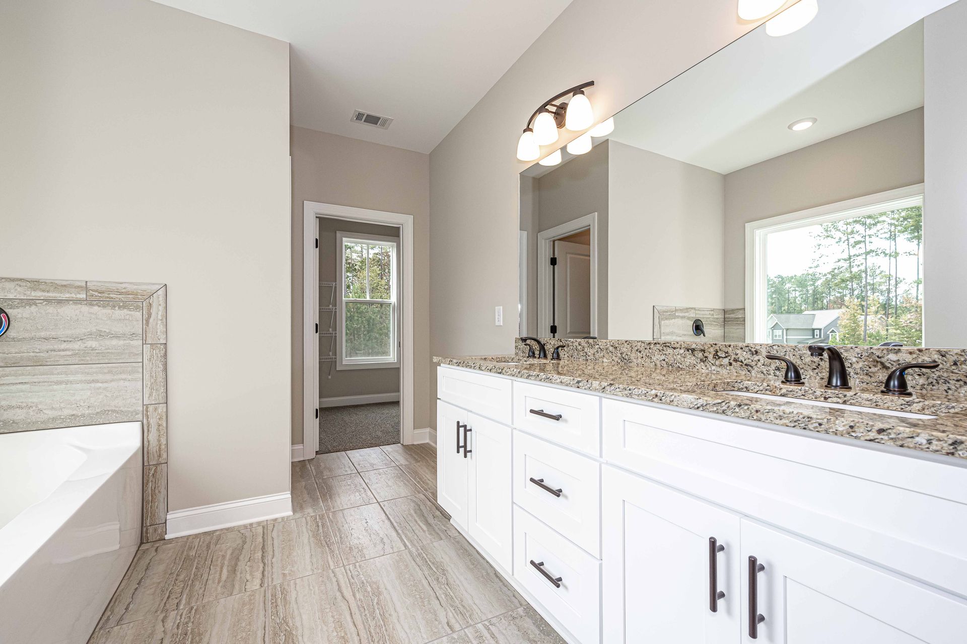 Bright modern bathroom with white vanity, granite countertop, large mirror, and walk-in shower.