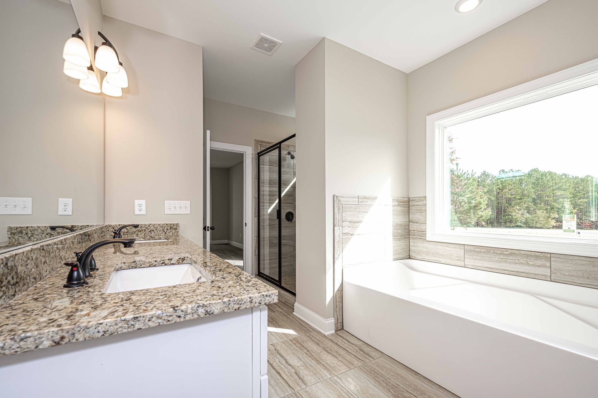 Bright modern bathroom with granite vanity, large window, and walk-in shower visible through the doorway