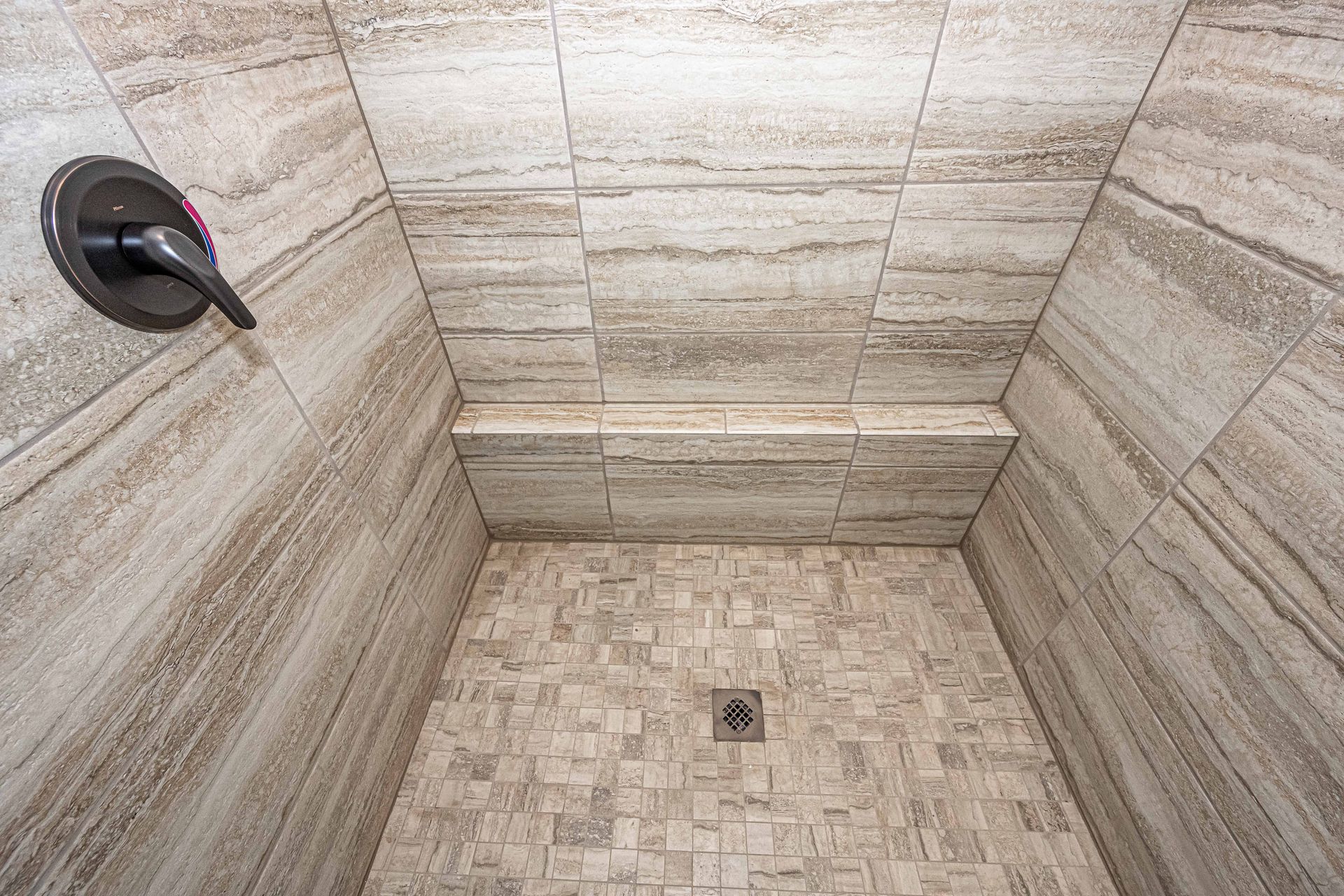 Beige tiled shower stall with a wall-mounted showerhead and floor drain