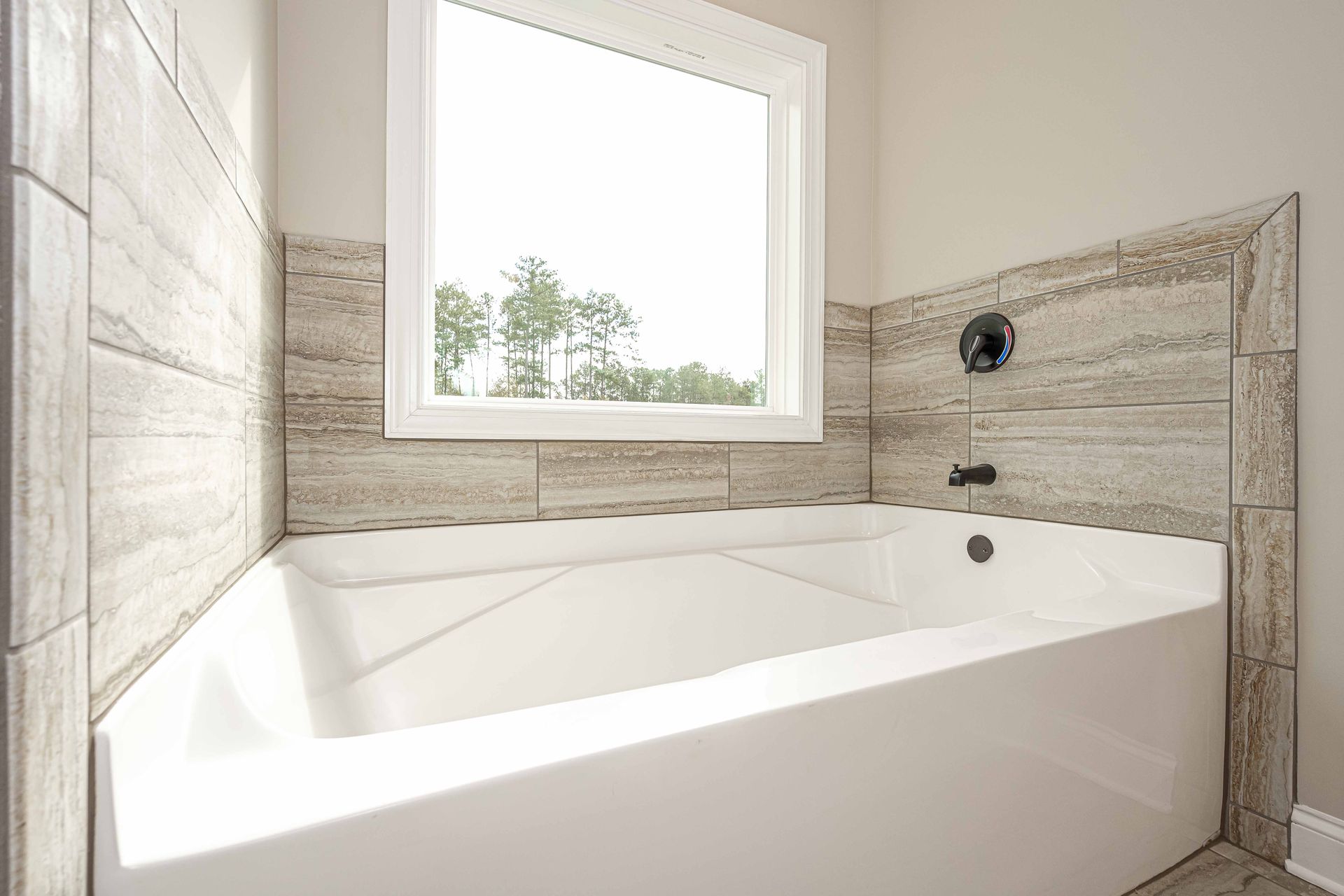 Modern white bathroom with a freestanding tub, stone tile walls, and a large window.