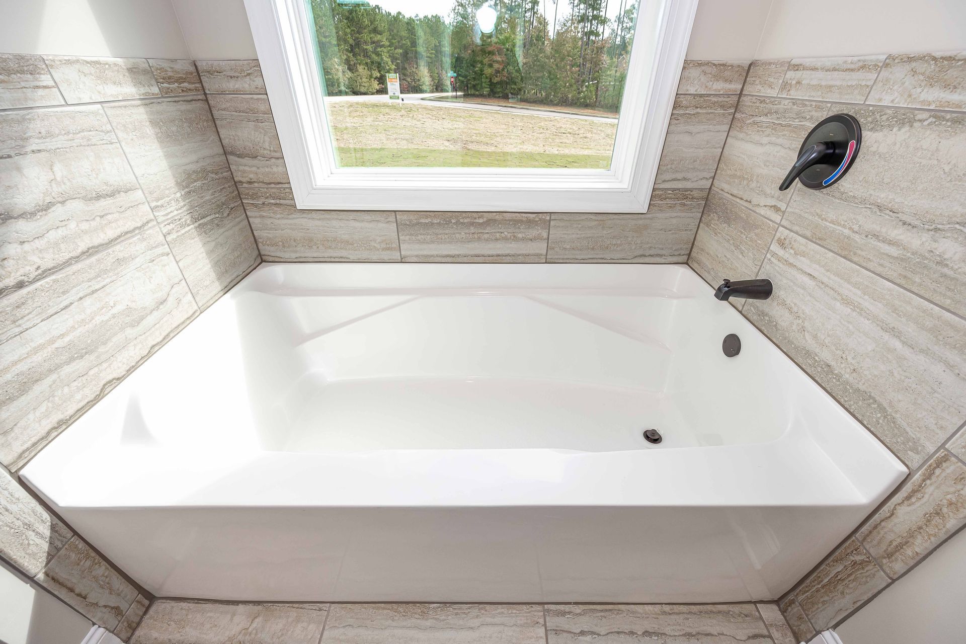 Bright white corner bathtub with beige tile walls beneath a window.