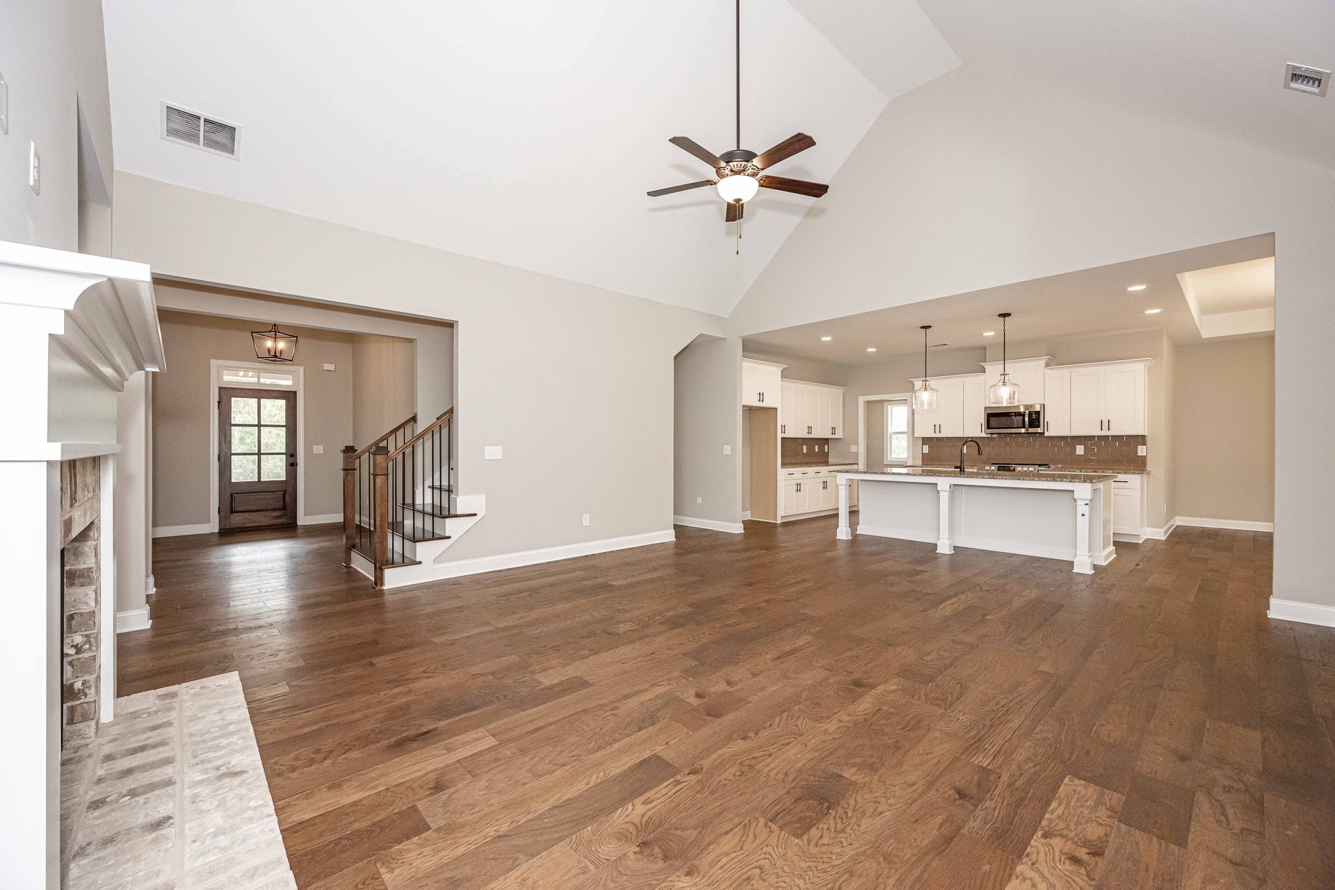 Spacious open-plan living room with hardwood floors, staircase, and bright white kitchen