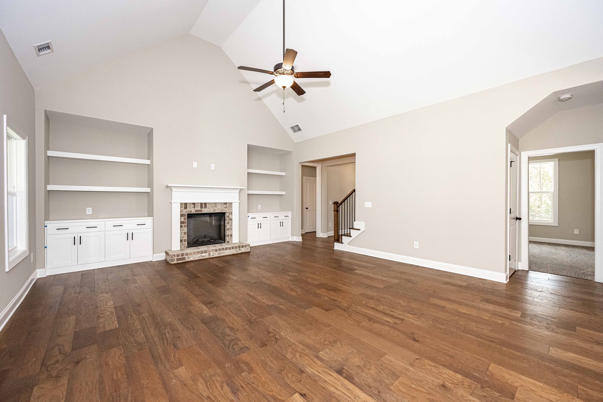 Spacious living room with hardwood floors, fireplace, built-in shelves, and a ceiling fan.