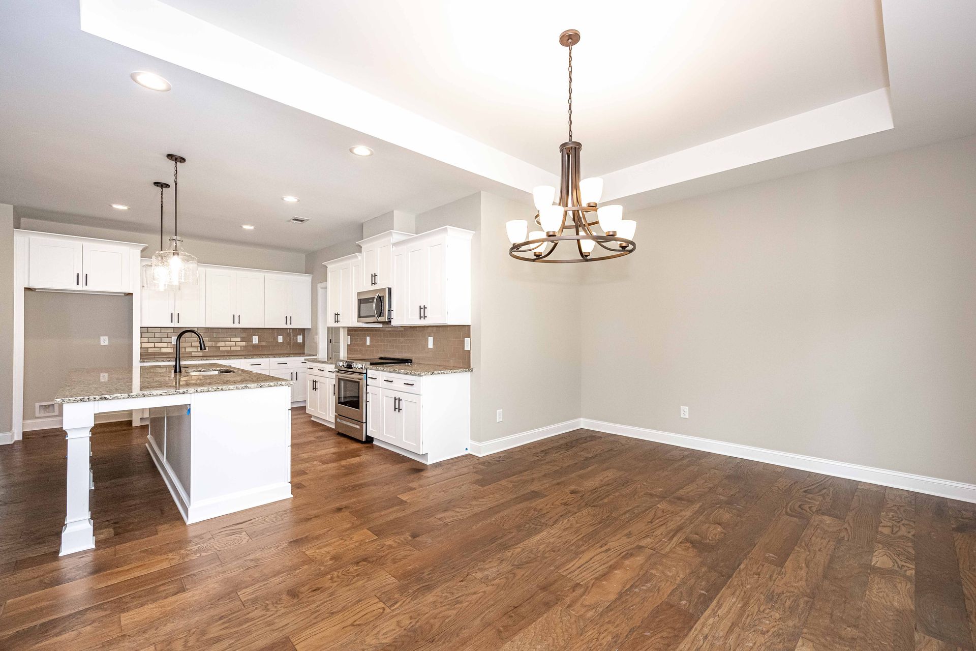 Bright open kitchen and dining area with white cabinets, wood floors, and a chandelier