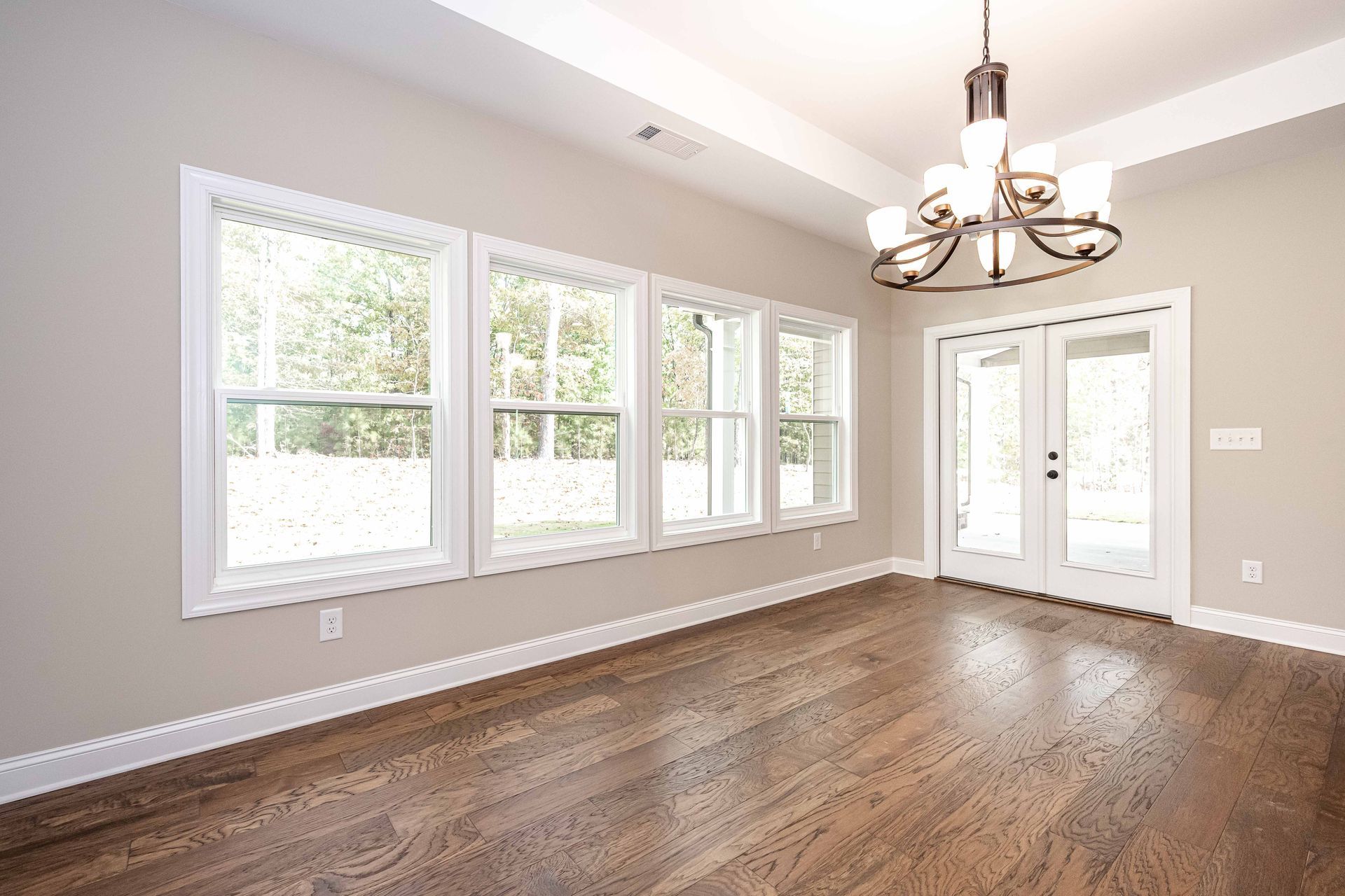 Empty dining room with hardwood floors, gray walls, large windows, and a chandelier