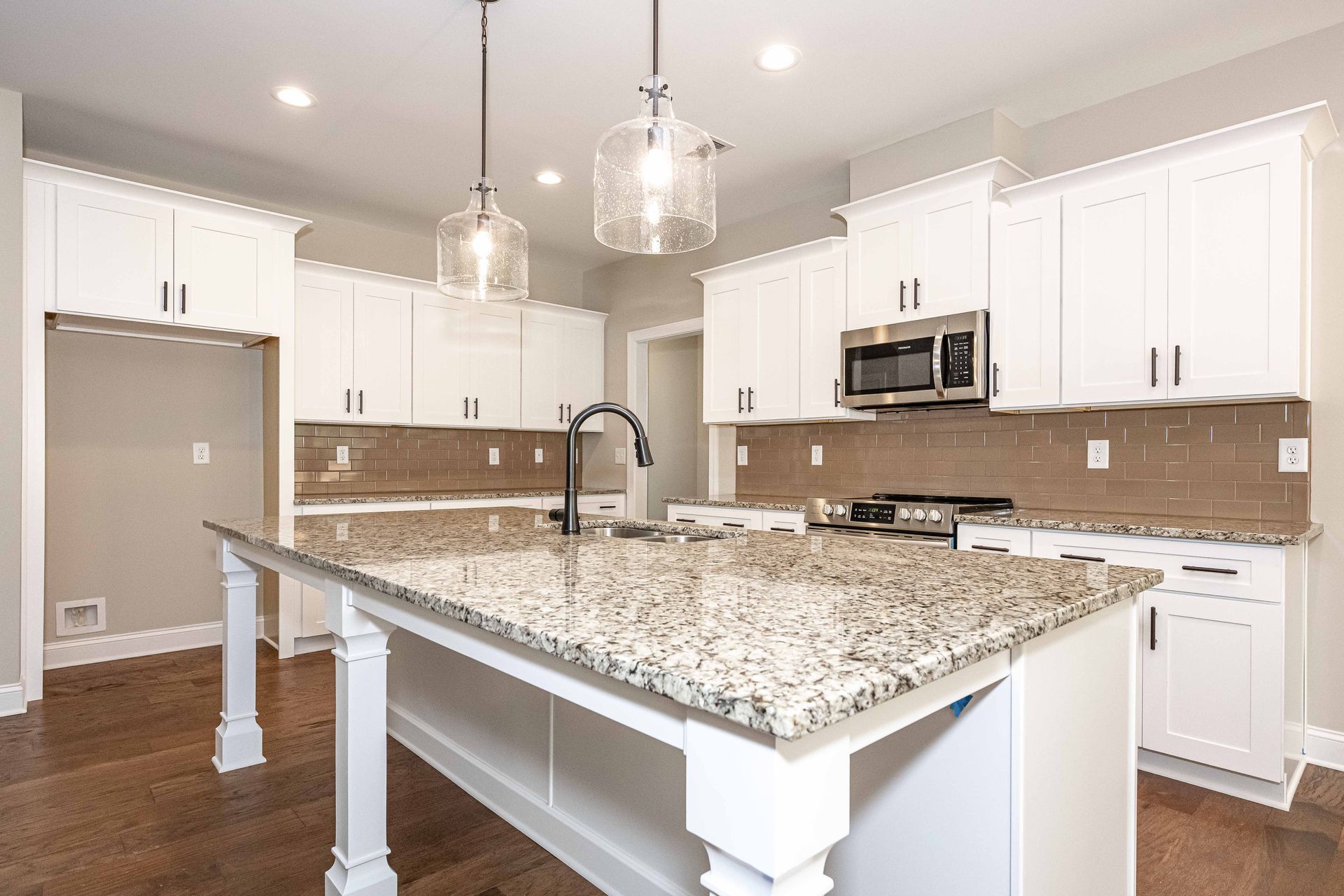 Bright modern kitchen with white cabinets, granite island, and stainless steel appliances