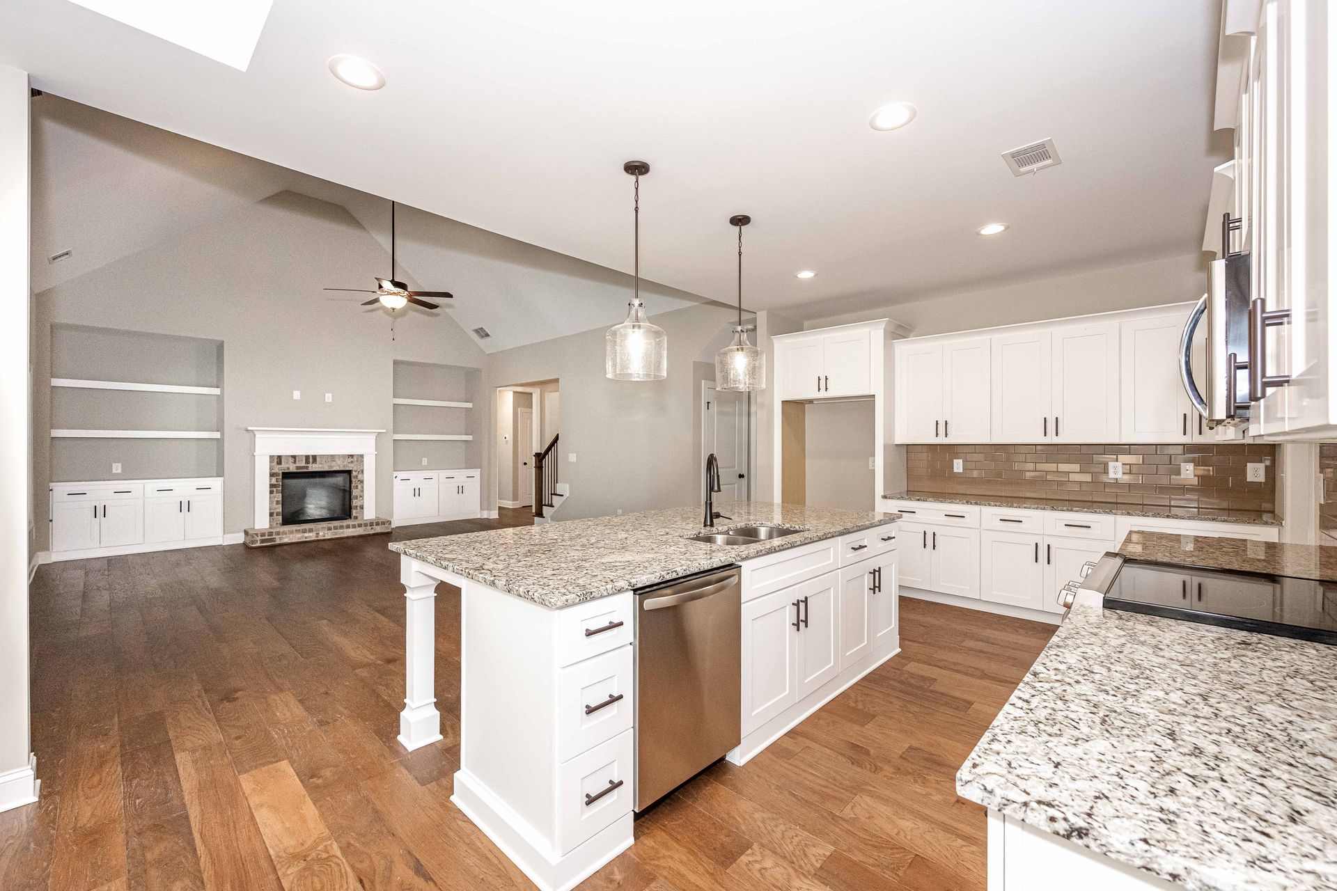 Bright modern kitchen with granite island, white cabinets, stainless appliances, and hardwood floors