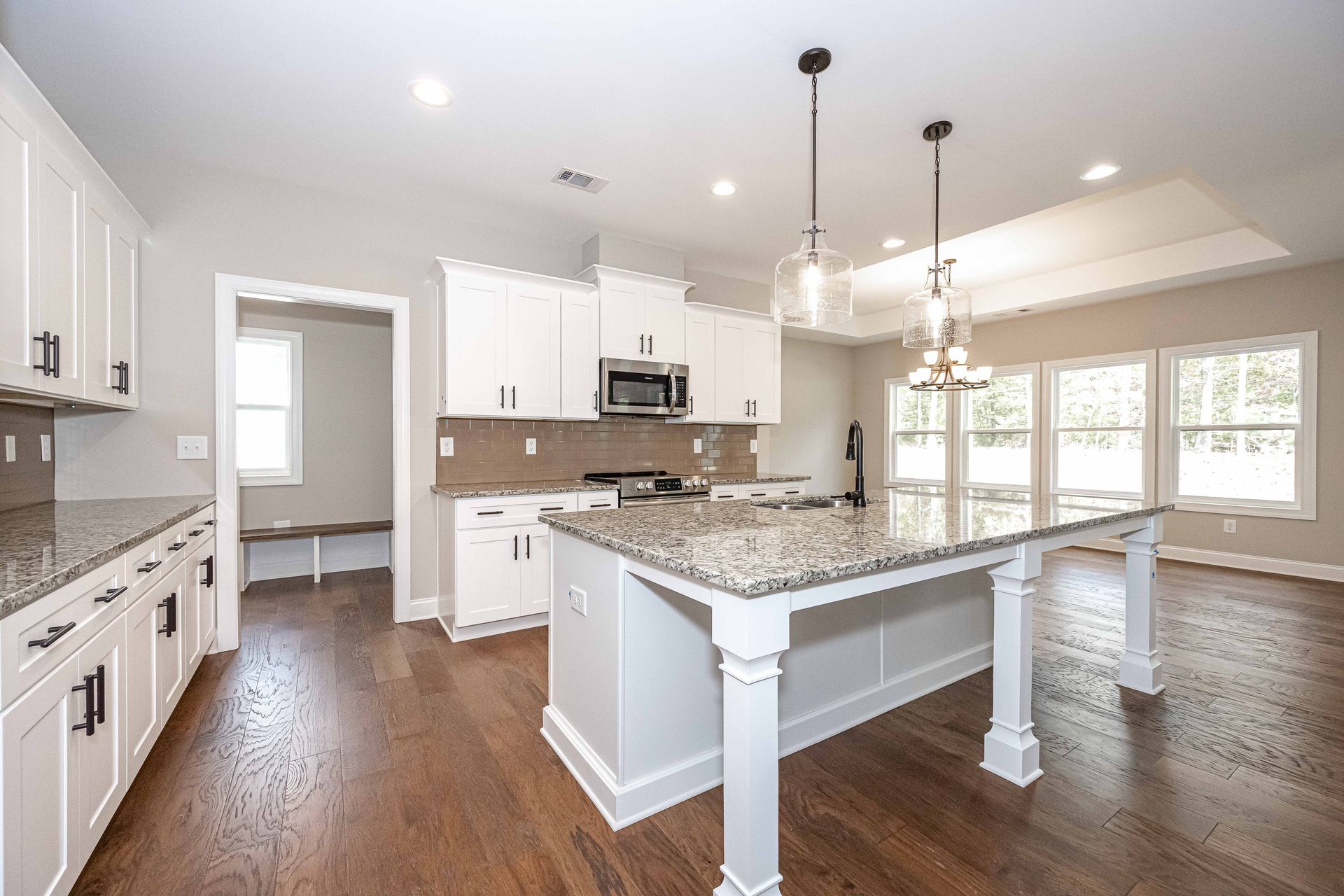 Bright modern kitchen with white cabinets, granite island, hardwood floors, and pendant lights