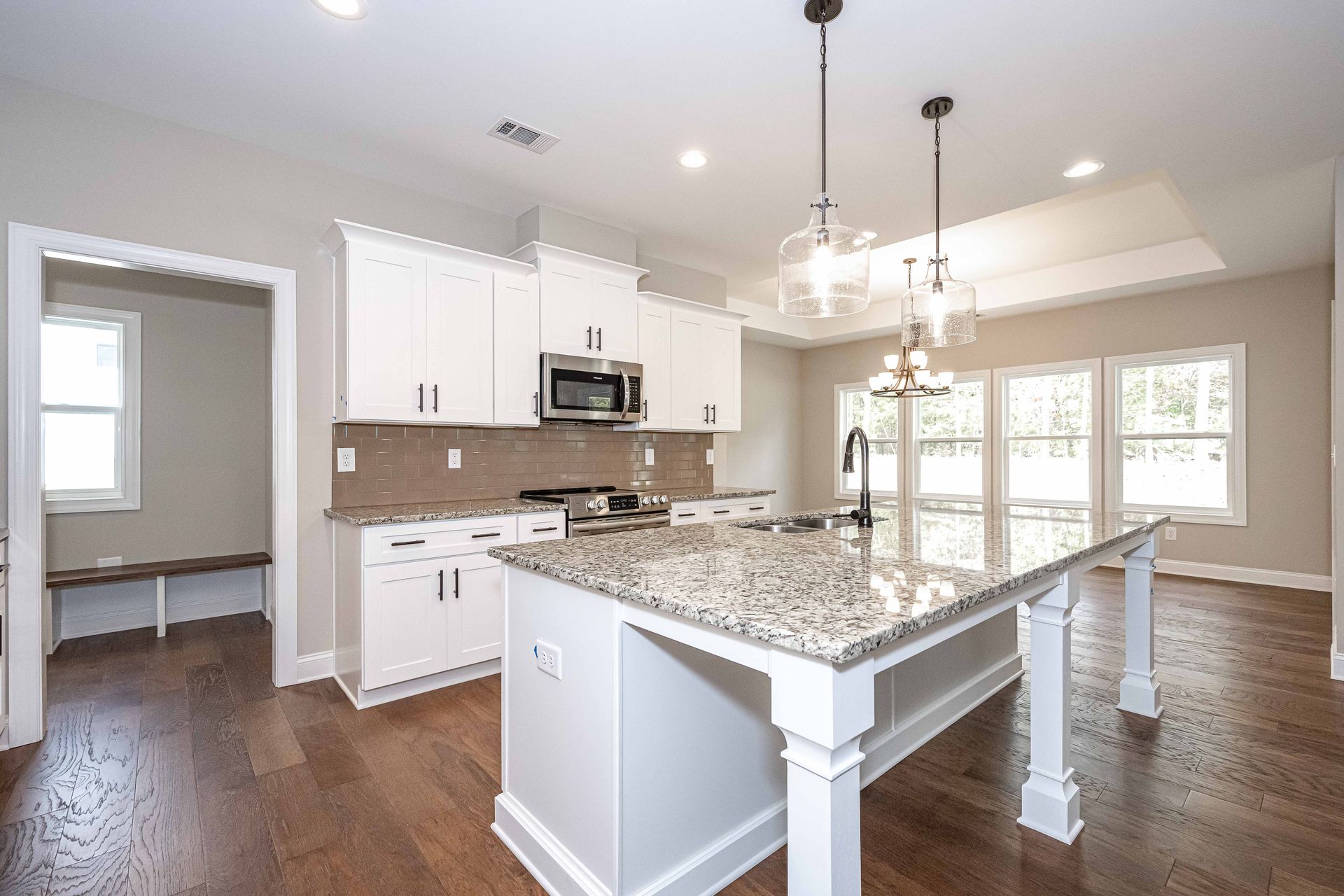 Bright, modern kitchen with white cabinets, granite island, stainless appliances, and hardwood floors
