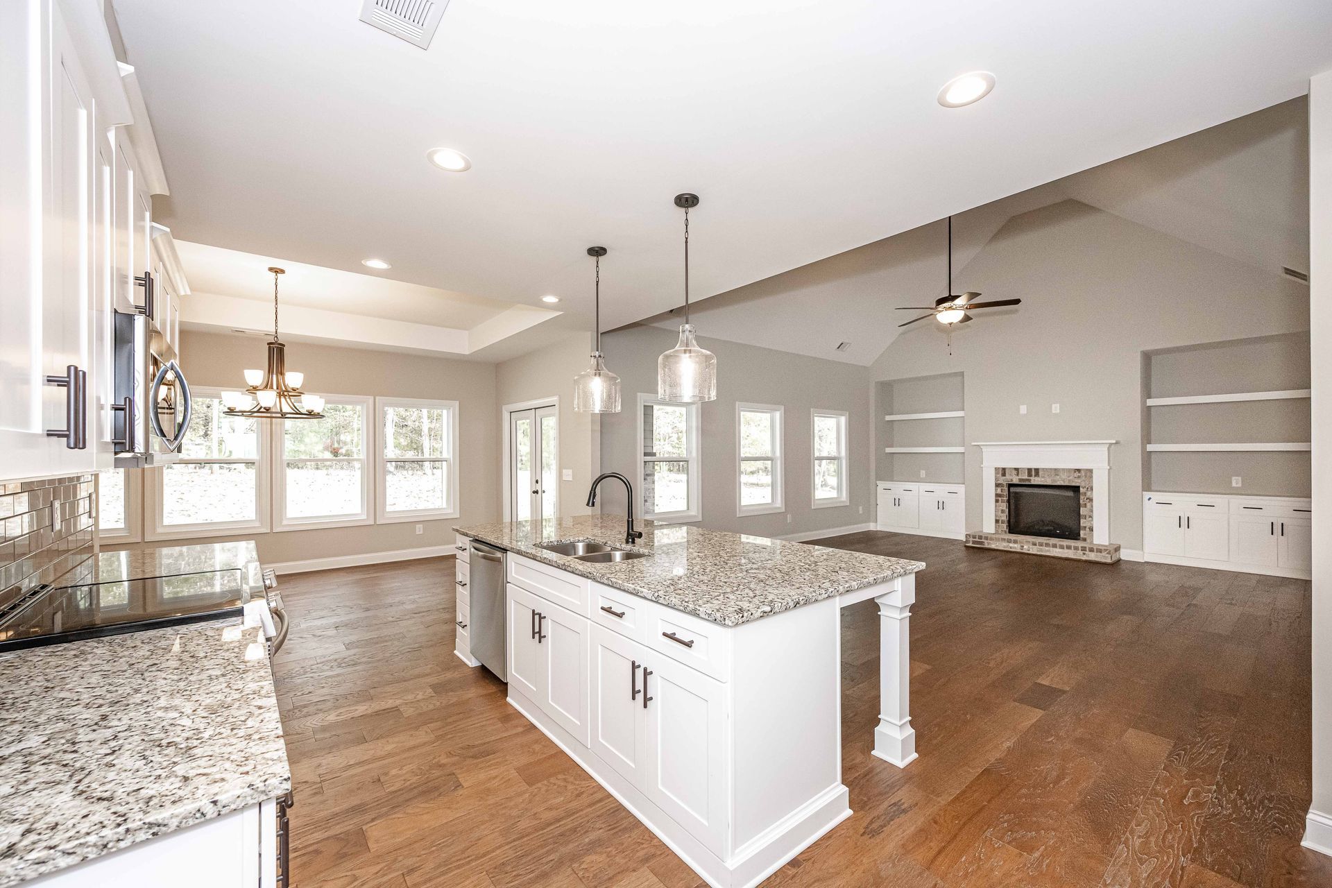 Bright open kitchen and living area with granite island, hardwood floors, and fireplace