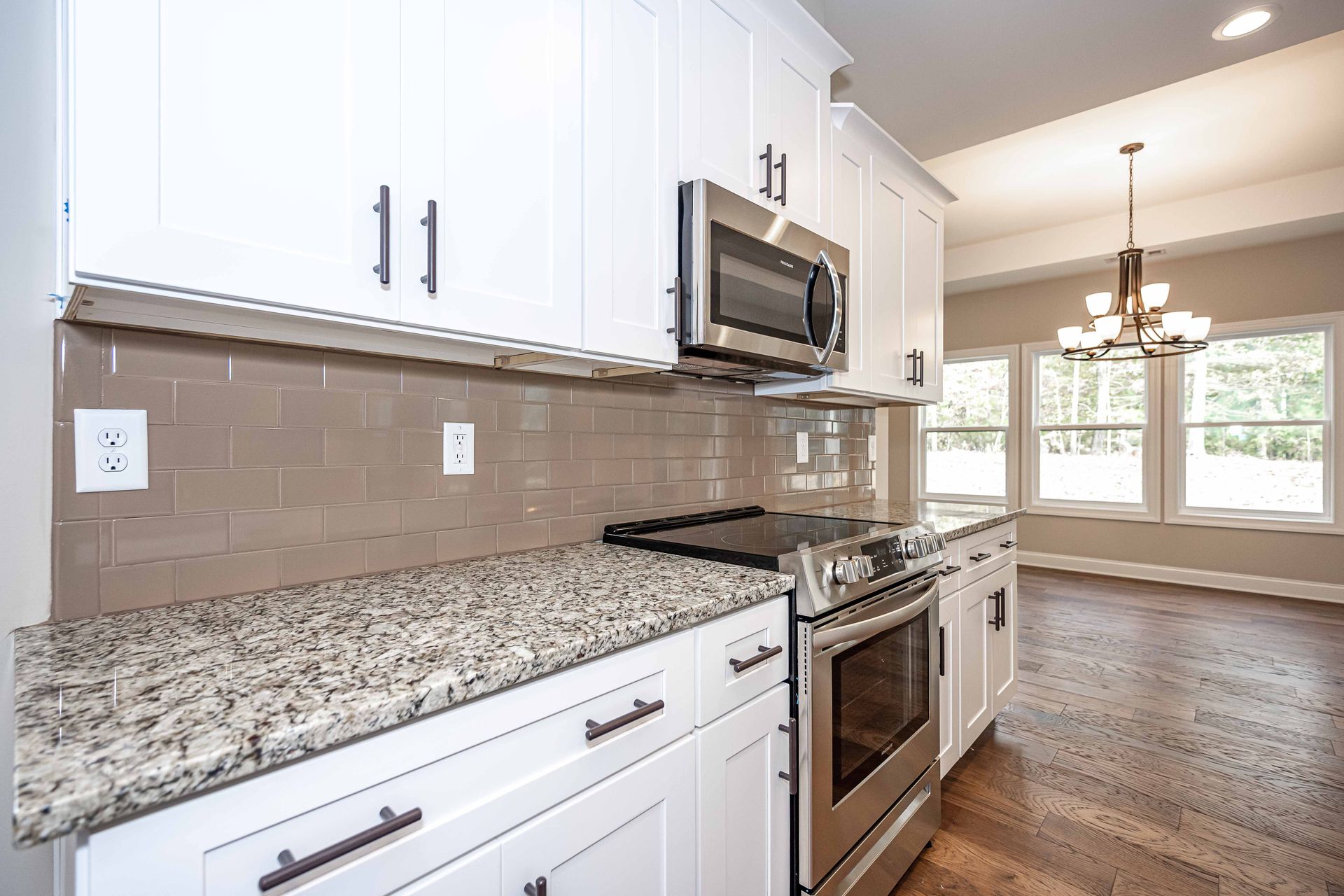 Bright modern kitchen with white cabinets, granite counters, stainless steel appliances, and hardwood floors
