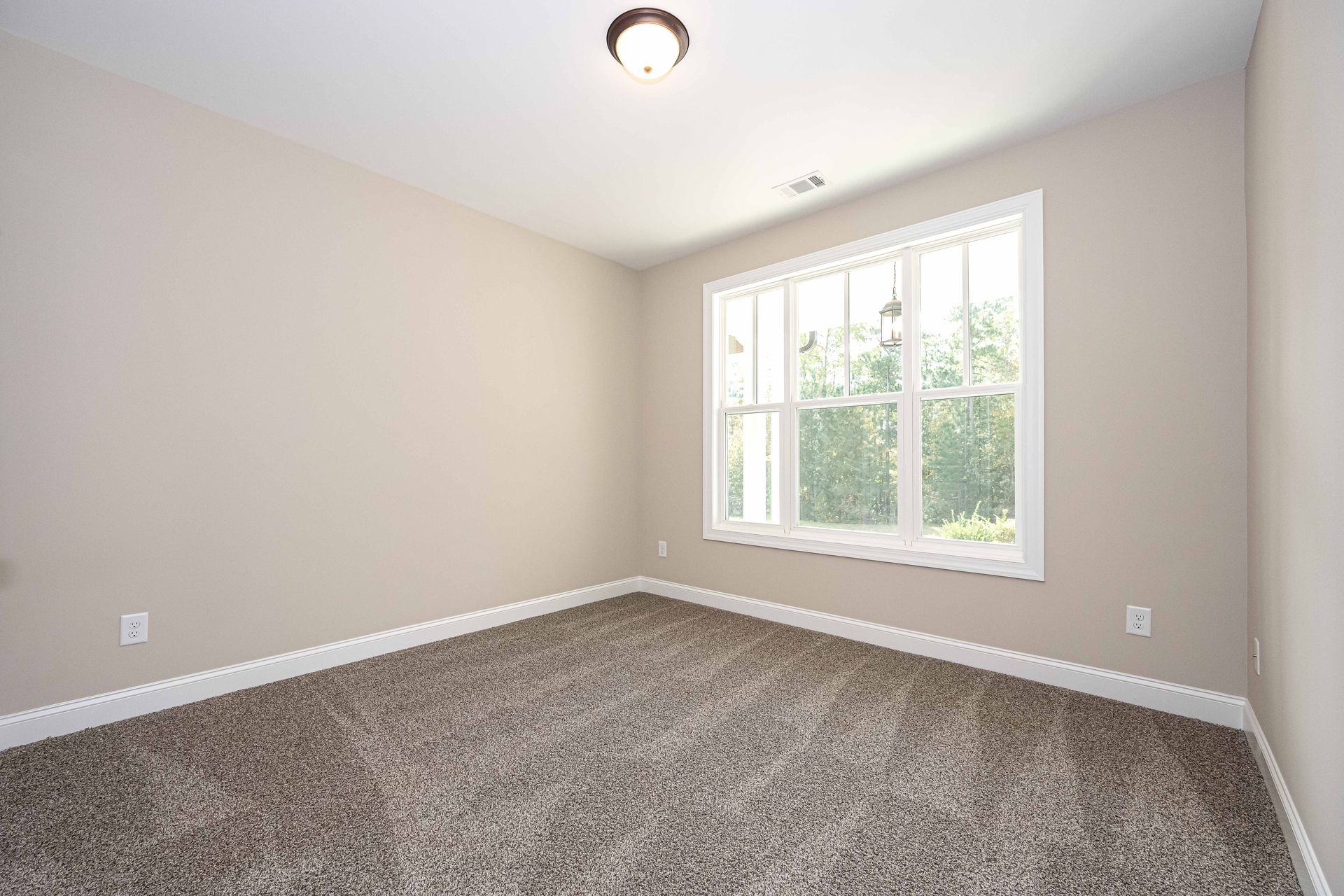 Empty beige bedroom with carpeted floor and a window letting in daylight.