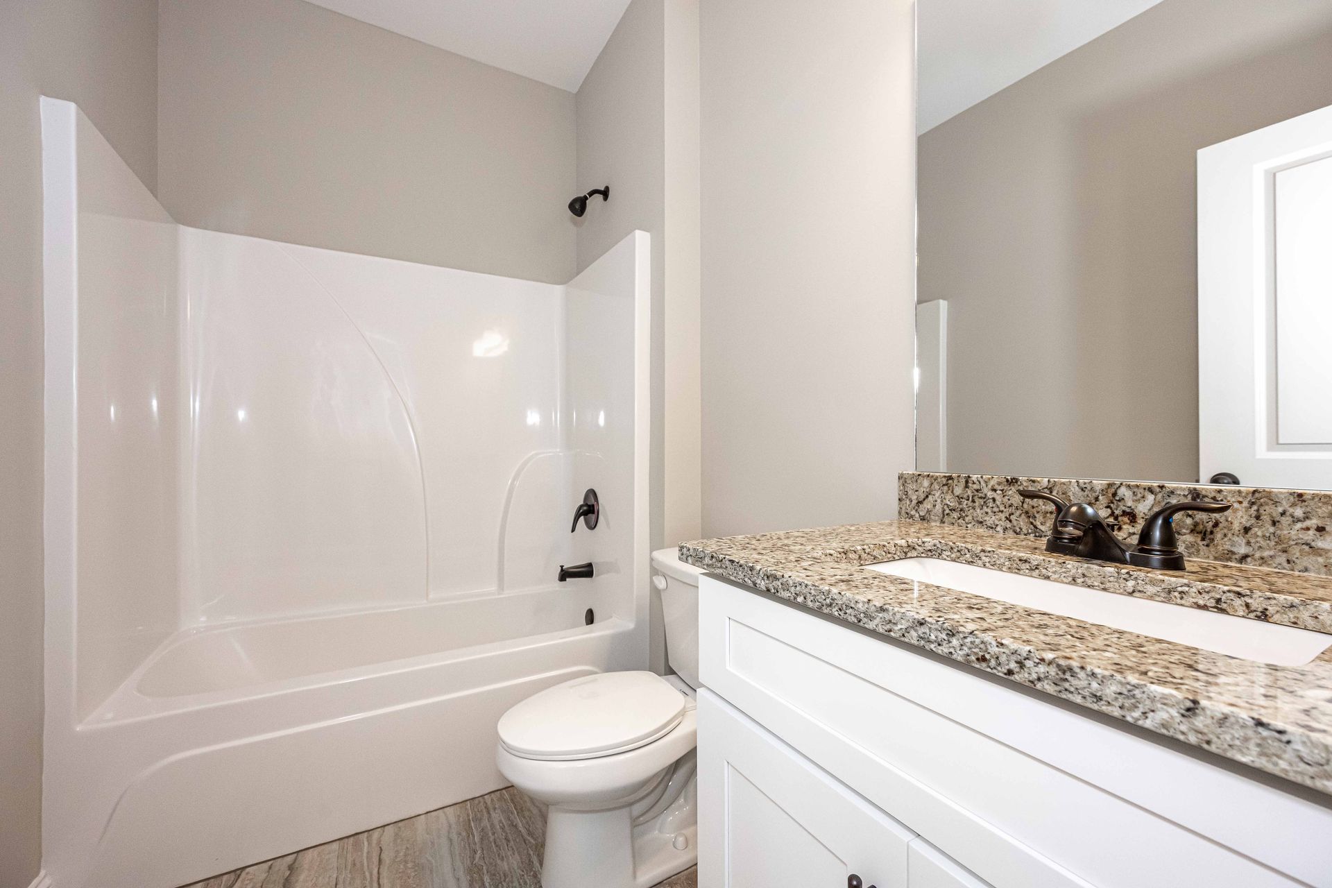 Bright bathroom with white tub, toilet, and granite vanity countertop near a window.