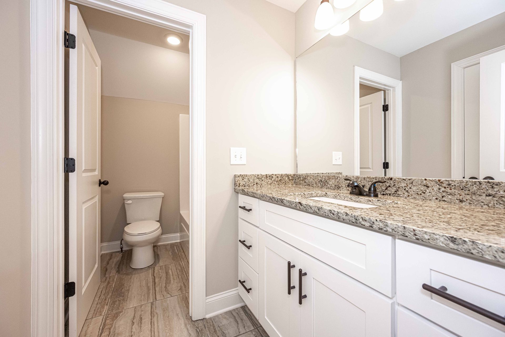 Modern bathroom vanity with granite countertop and mirror, view into a separate toilet room