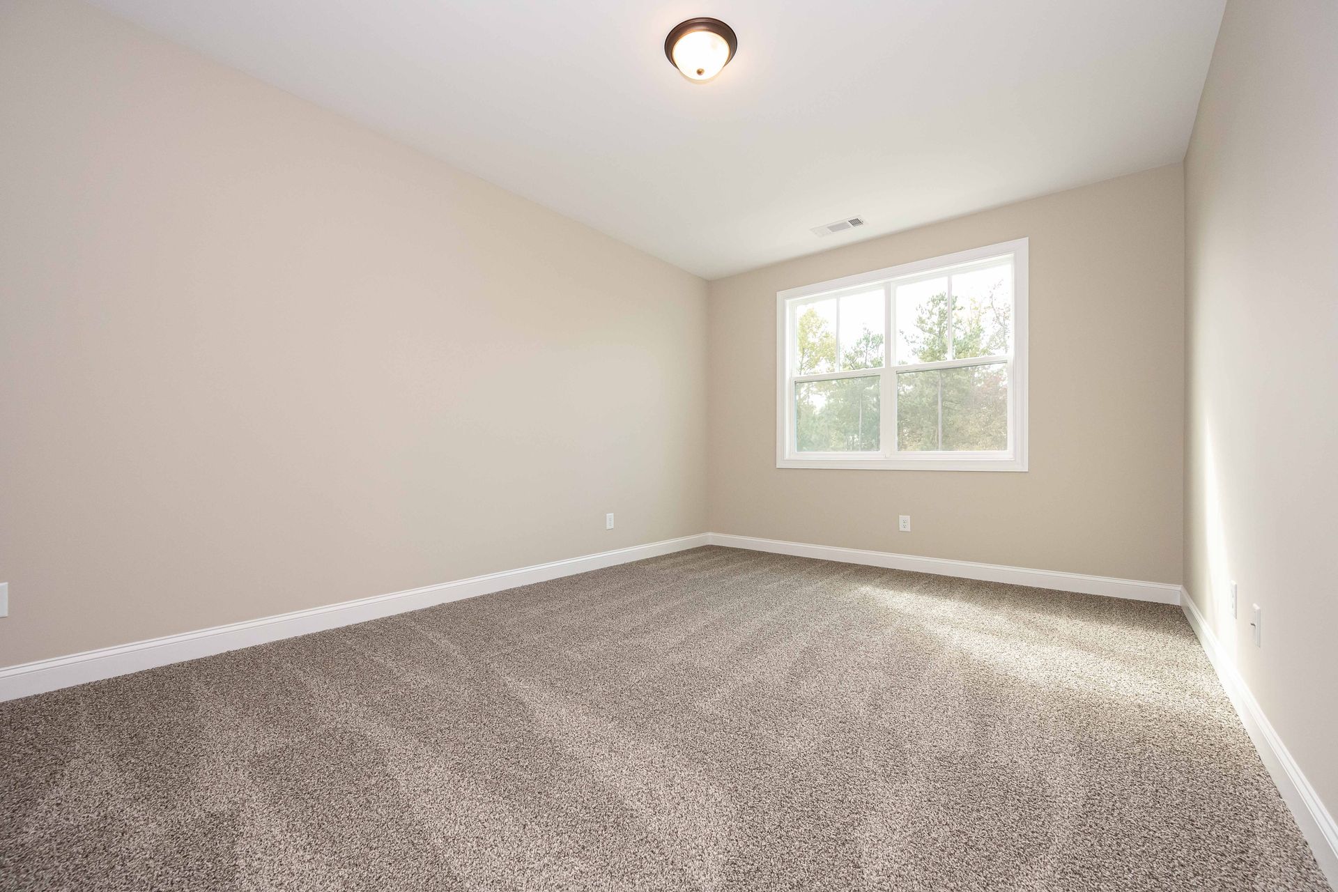Empty beige bedroom with carpeted floor and a window letting in daylight