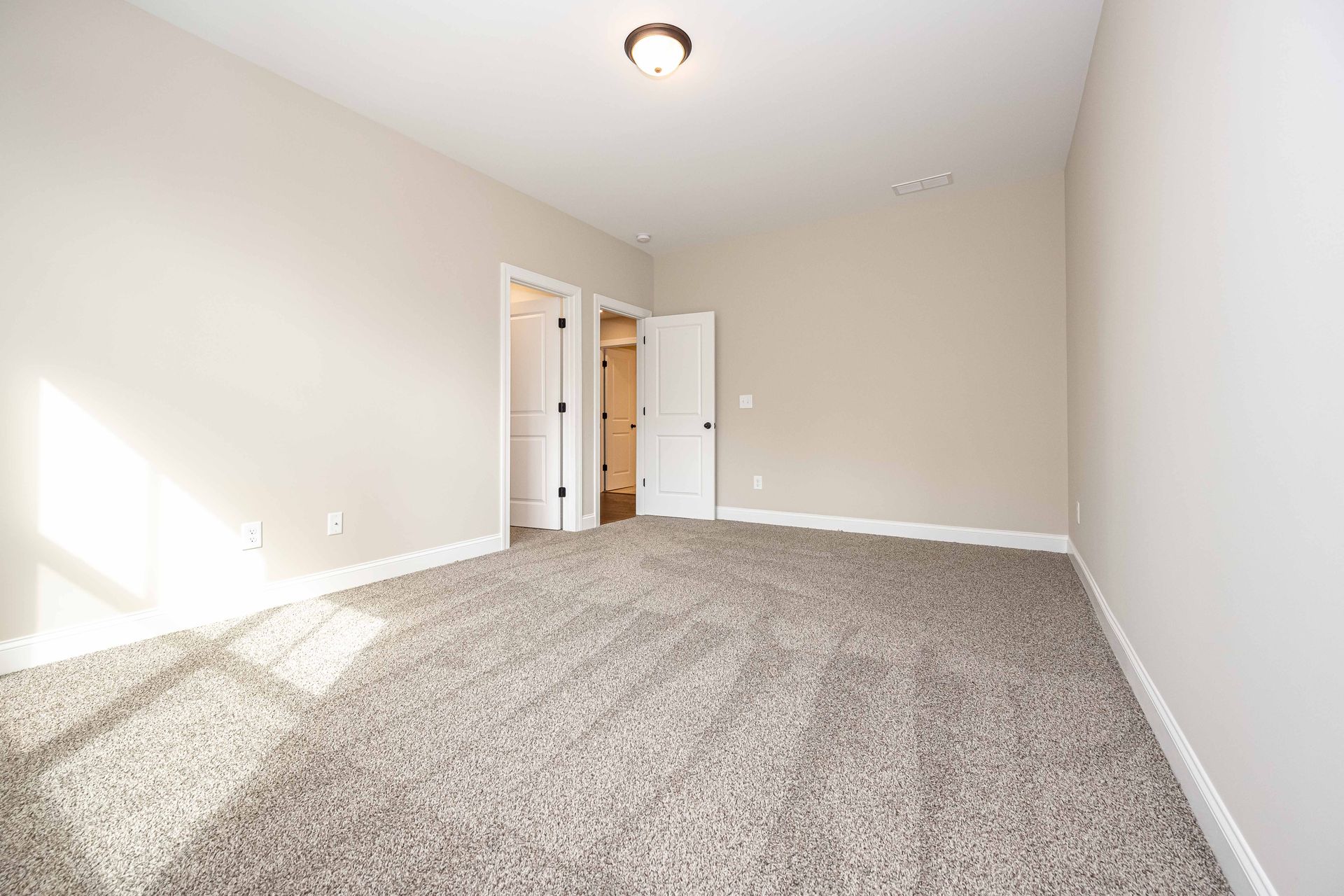Empty beige bedroom with carpet, open closet doors, and a ceiling light.