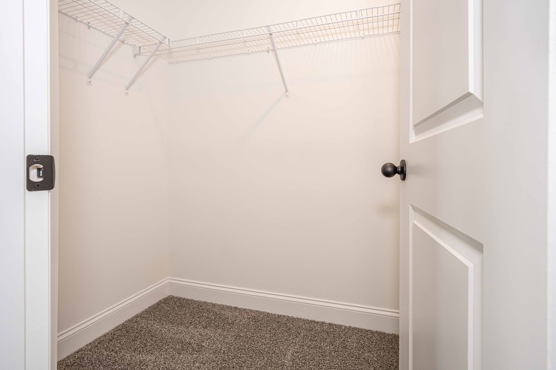Empty walk-in closet with white walls, wire shelving, and beige carpet, viewed through an open door