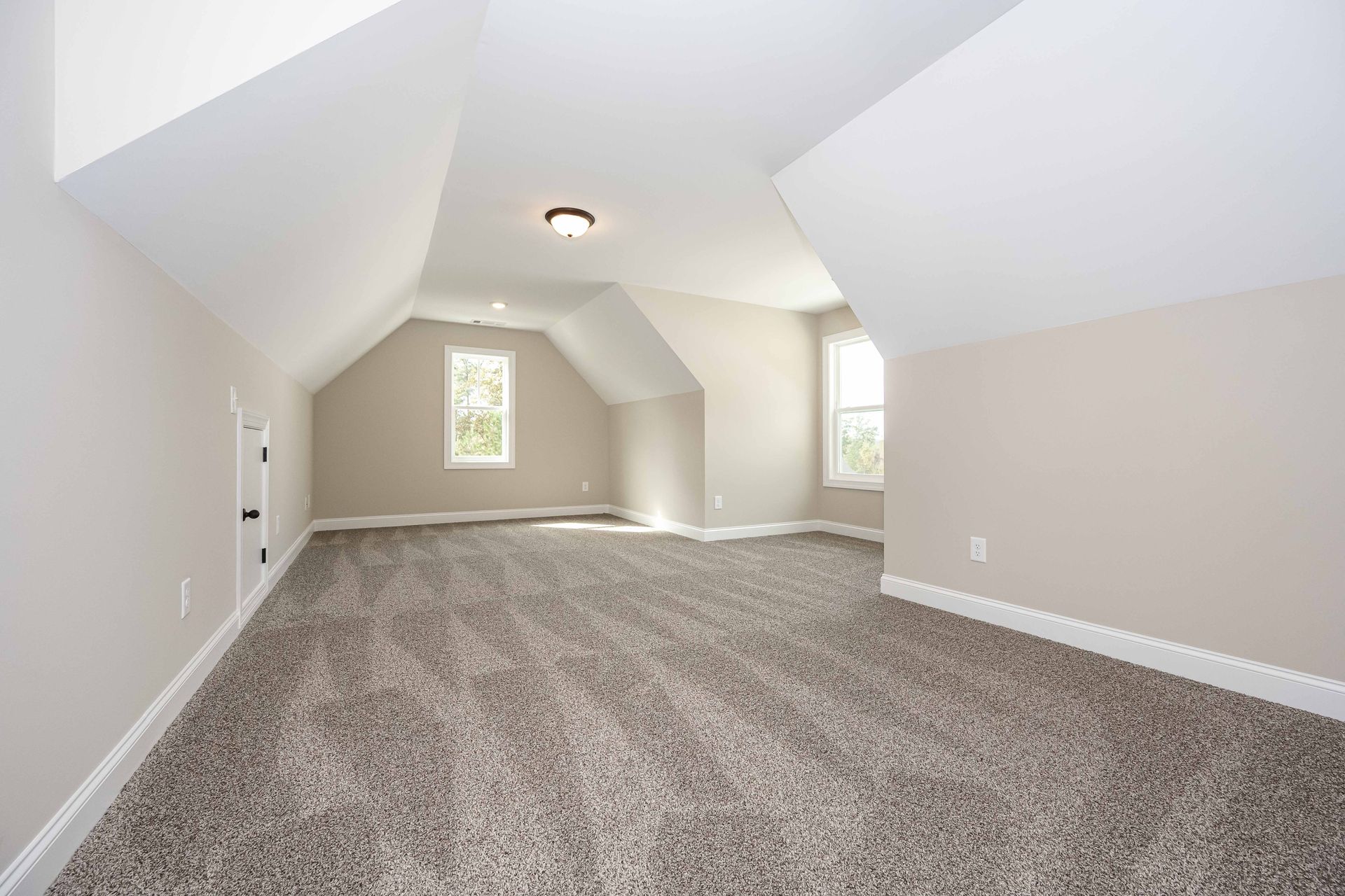 Empty carpeted attic room with sloped white ceiling and two small windows