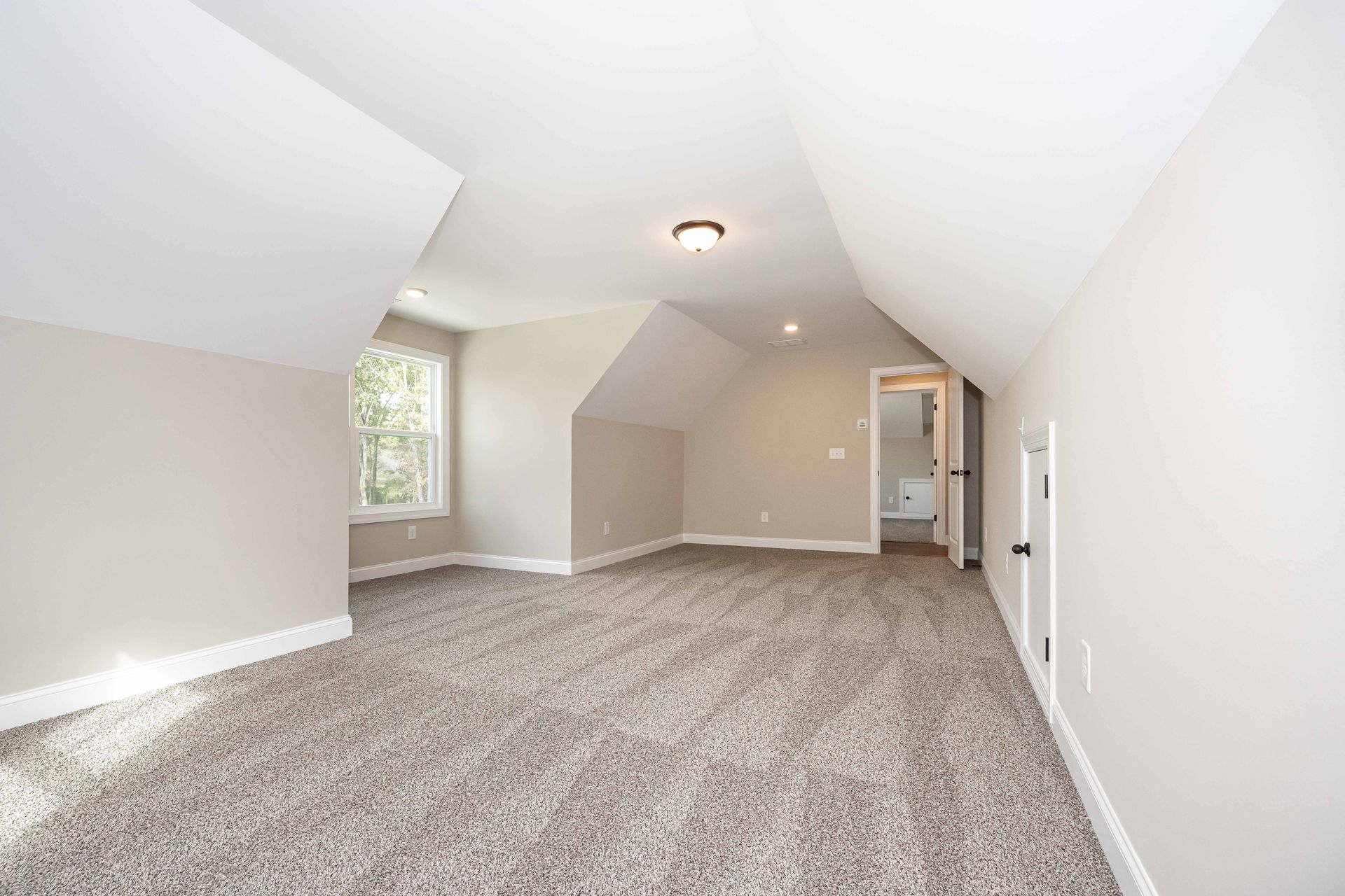 Empty carpeted attic bedroom with sloped white ceilings, skylight, and a doorway to a small bathroom