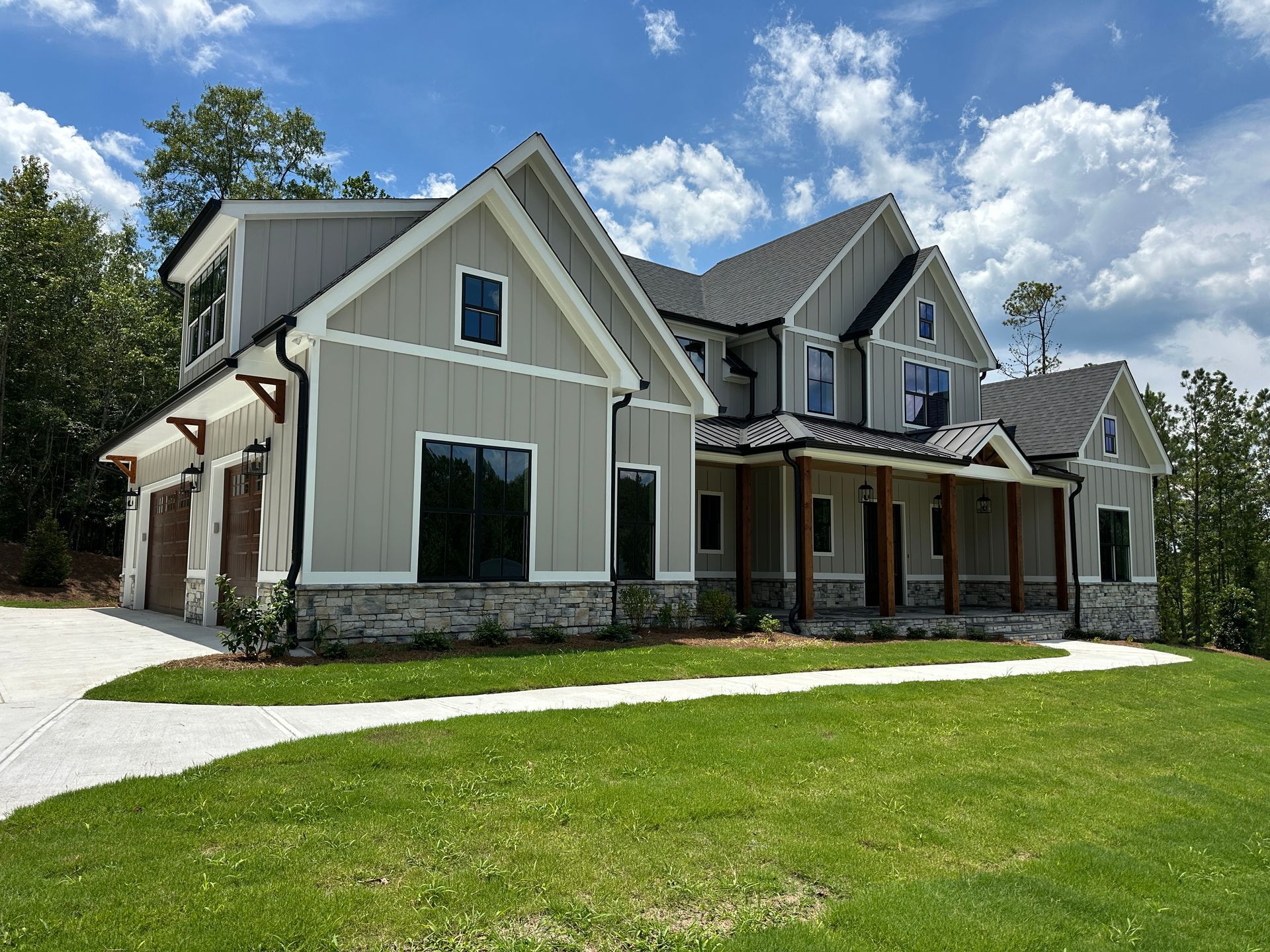 Large beige suburban house with stone accents and a green lawn under a partly cloudy blue sky