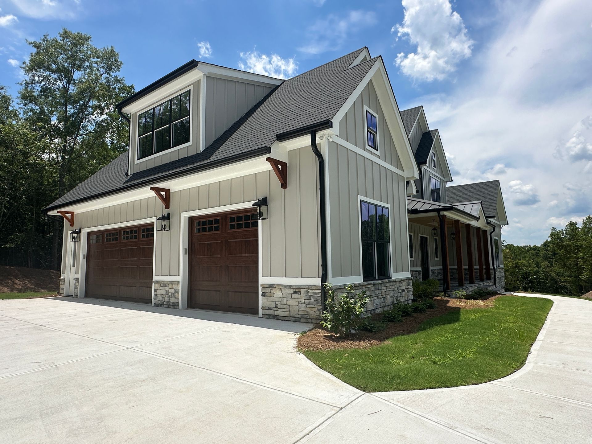 Modern gray house with three garage doors, stone trim, and a paved driveway under a blue sky