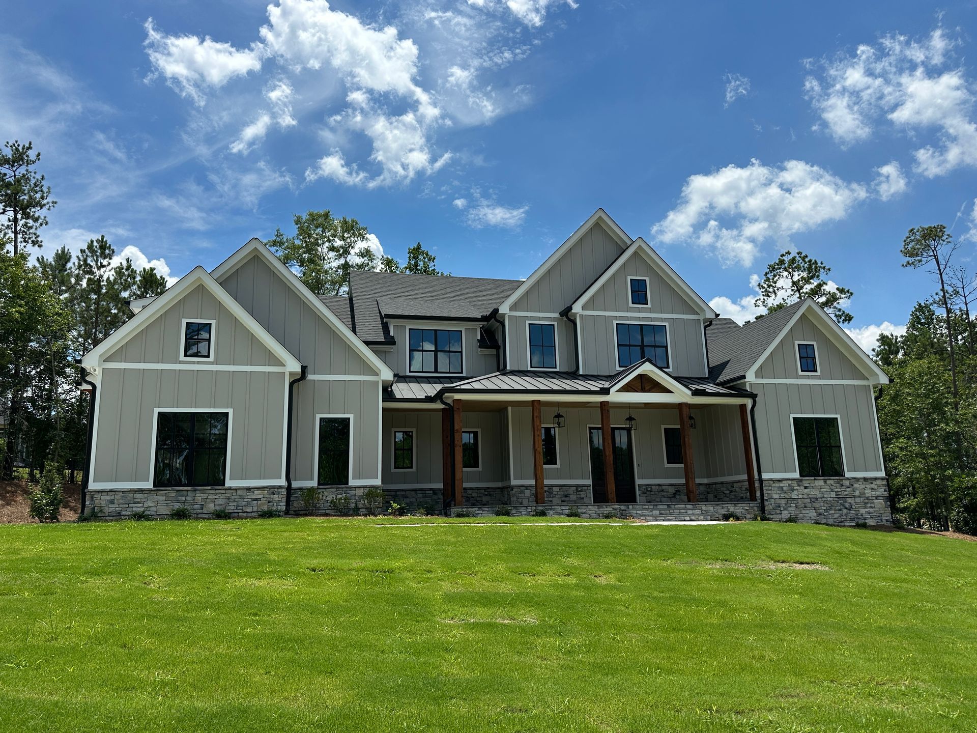 Large beige suburban house with stone accents and a front porch under a bright blue sky, viewed from the lawn