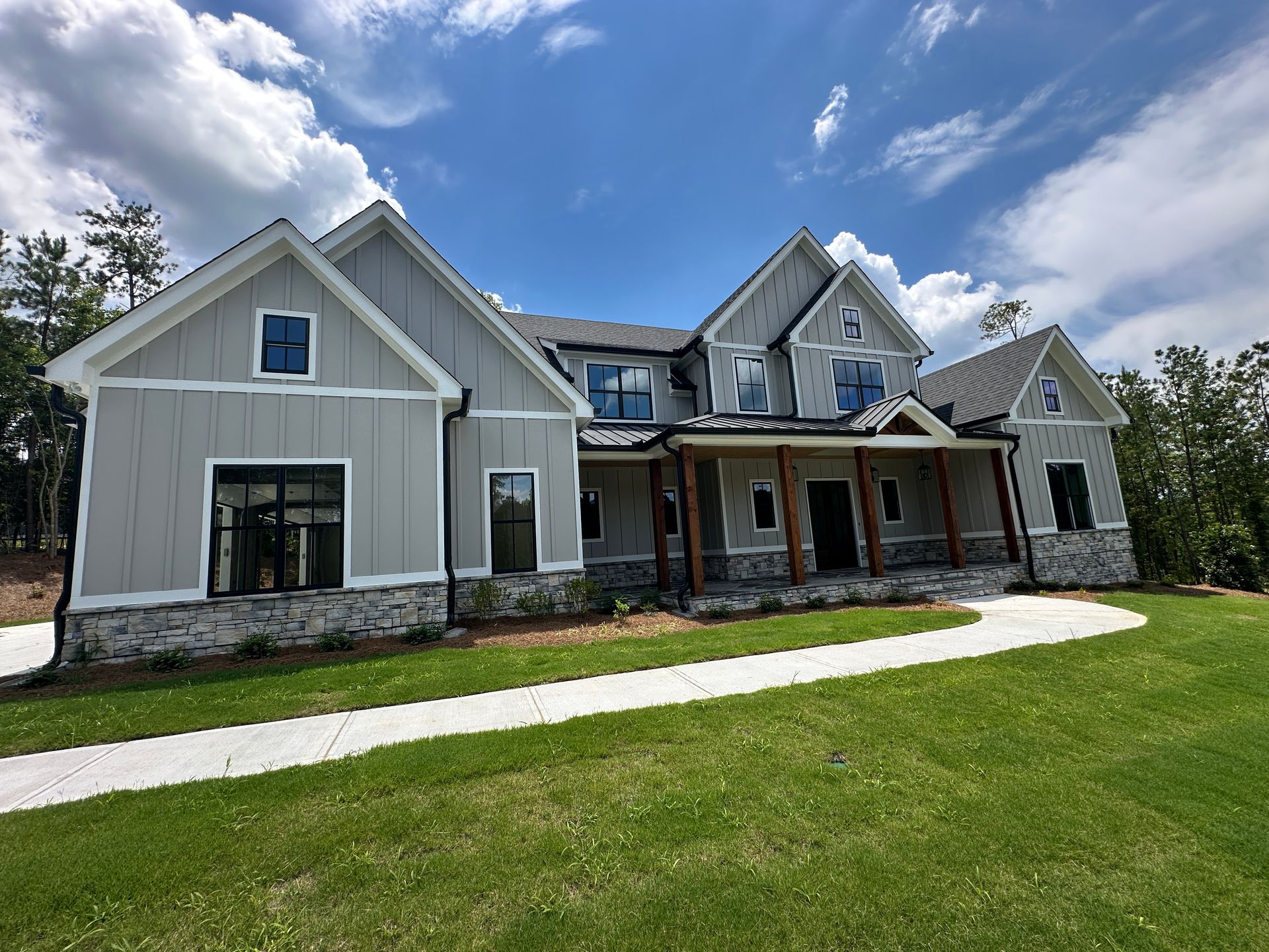 Large gray suburban house with stone accents, front porch, and a green lawn under a blue sky