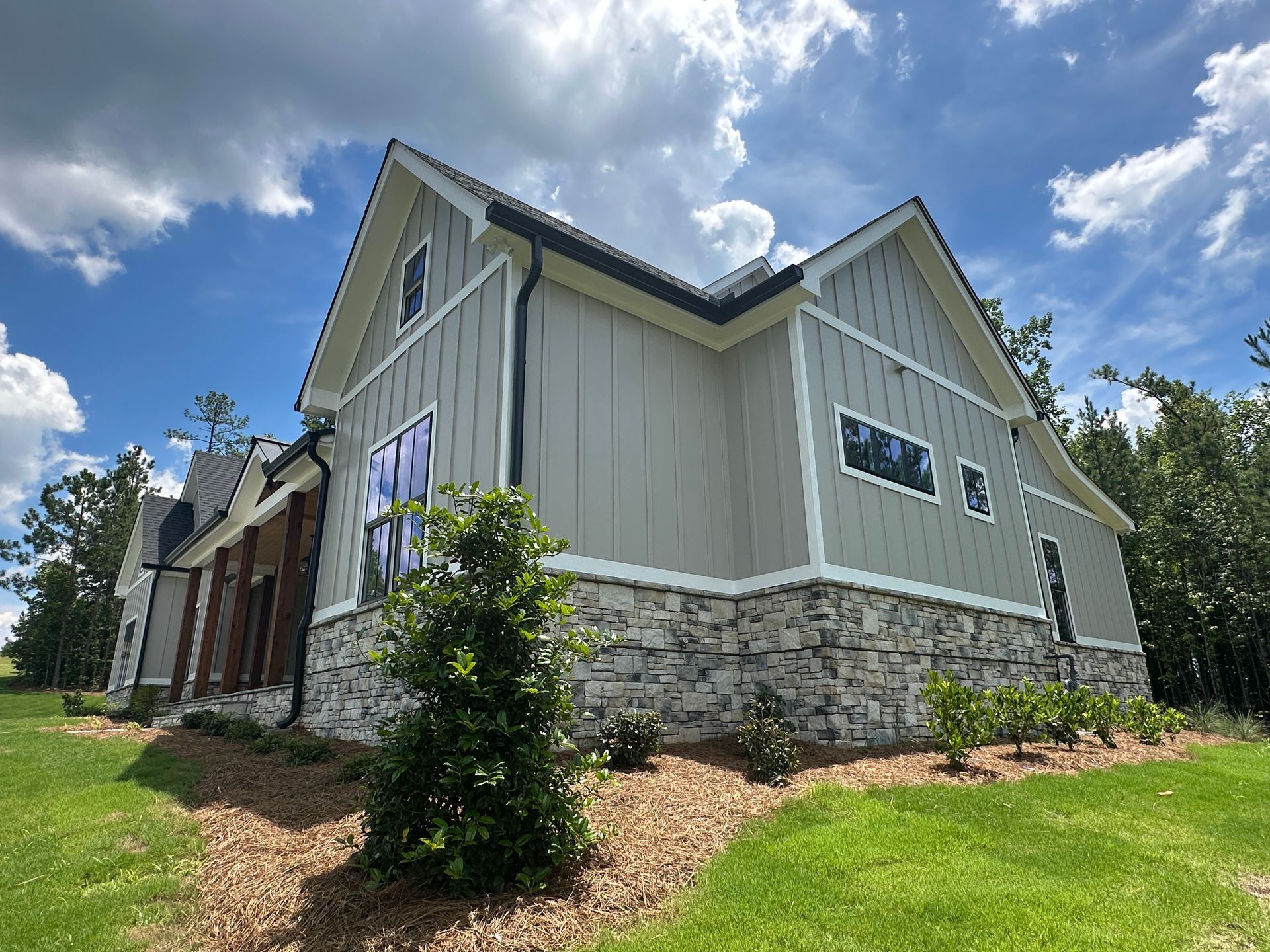 Modern house exterior with gray siding, stone foundation, and cloudy blue sky above a landscaped yard