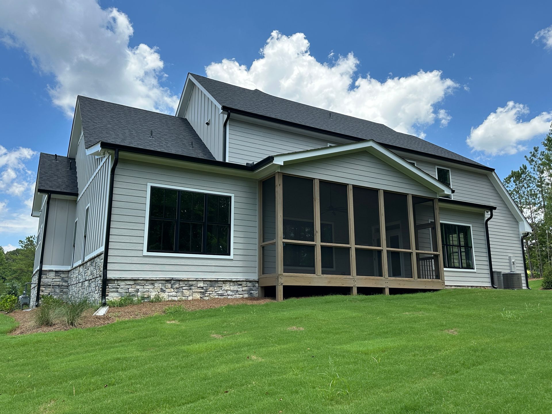 White house with gray roof and screened porch on a grassy hill under a blue sky