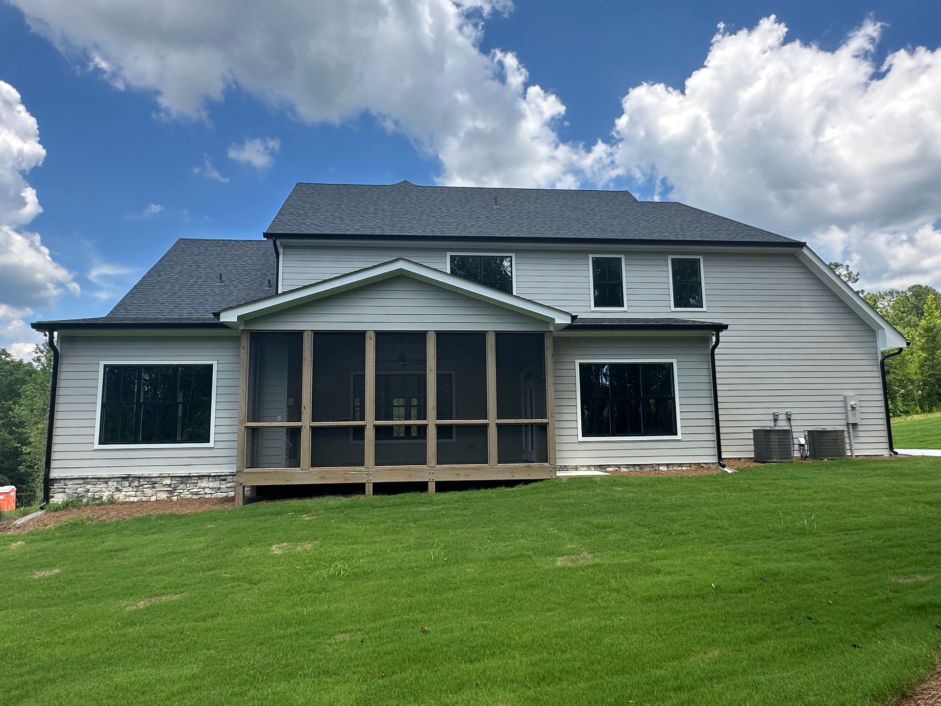 White house with screened porch and dark roof on a green lawn under a cloudy blue sky
