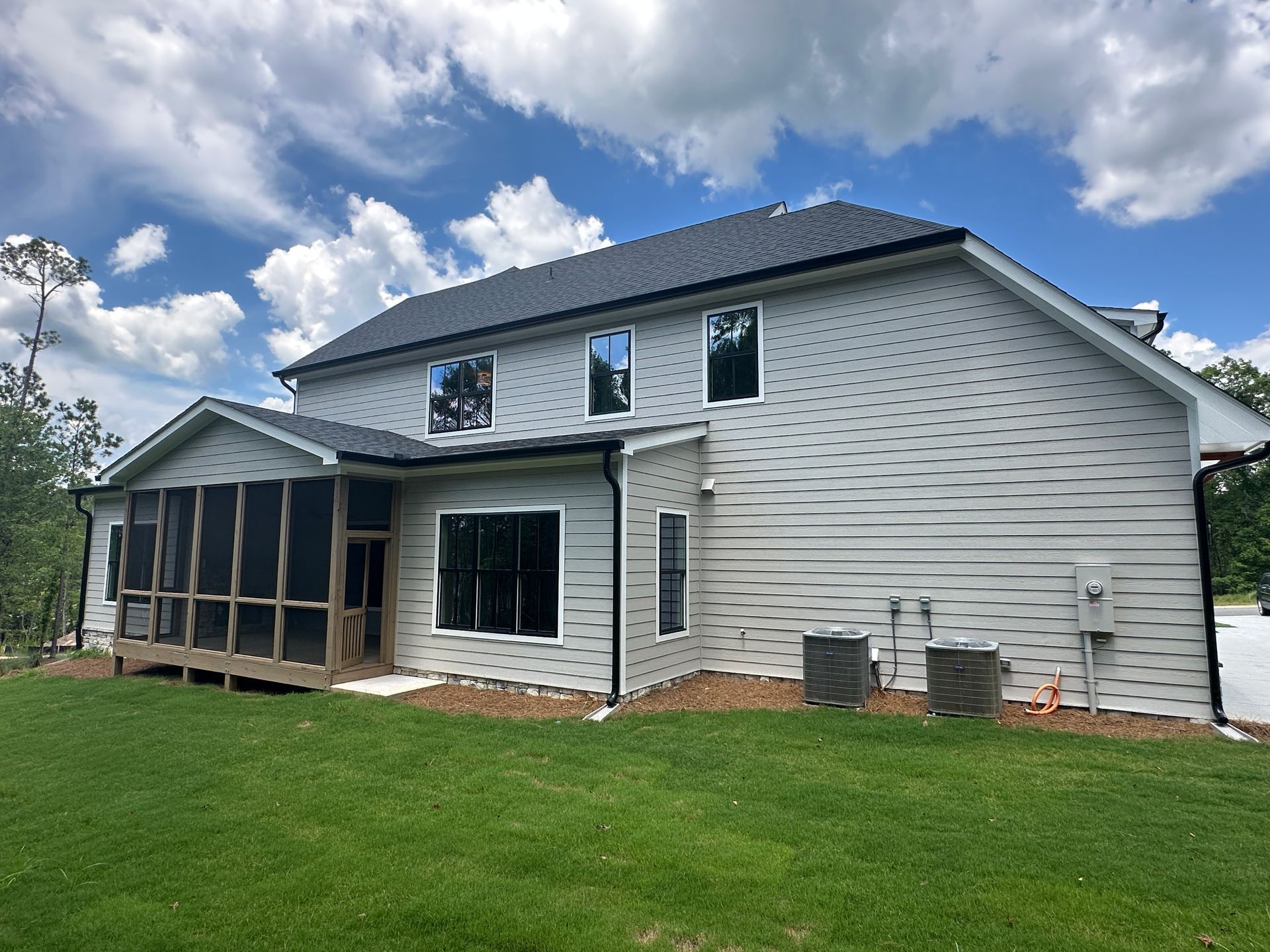 Back of a white two-story house with screened porch and green lawn under a blue sky