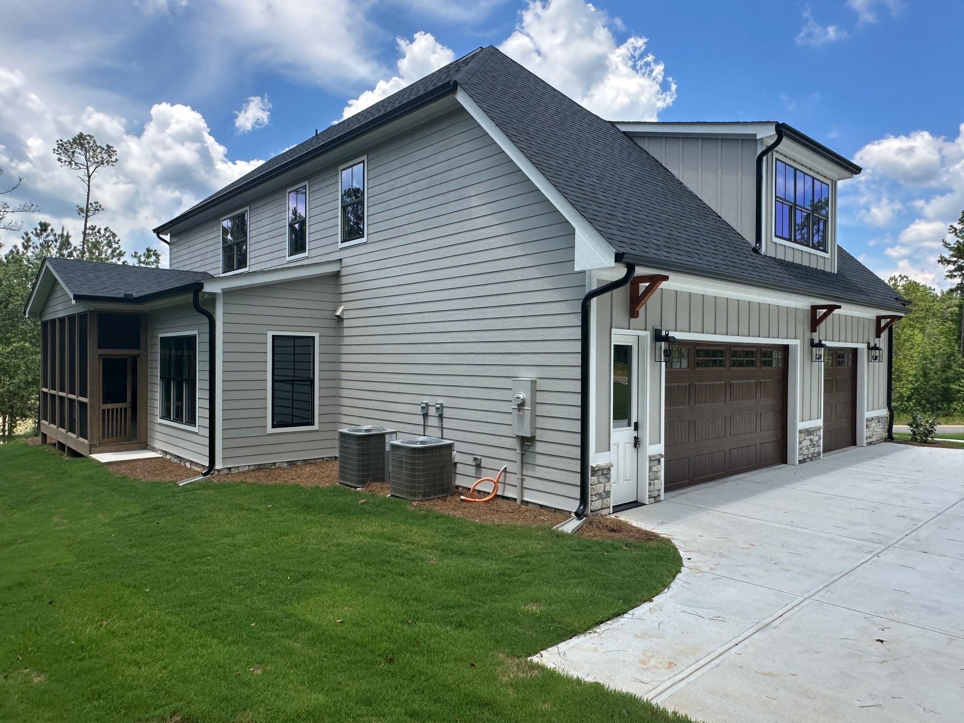 Suburban house exterior with gray siding, garage, and concrete driveway on a green lawn under a partly cloudy sky