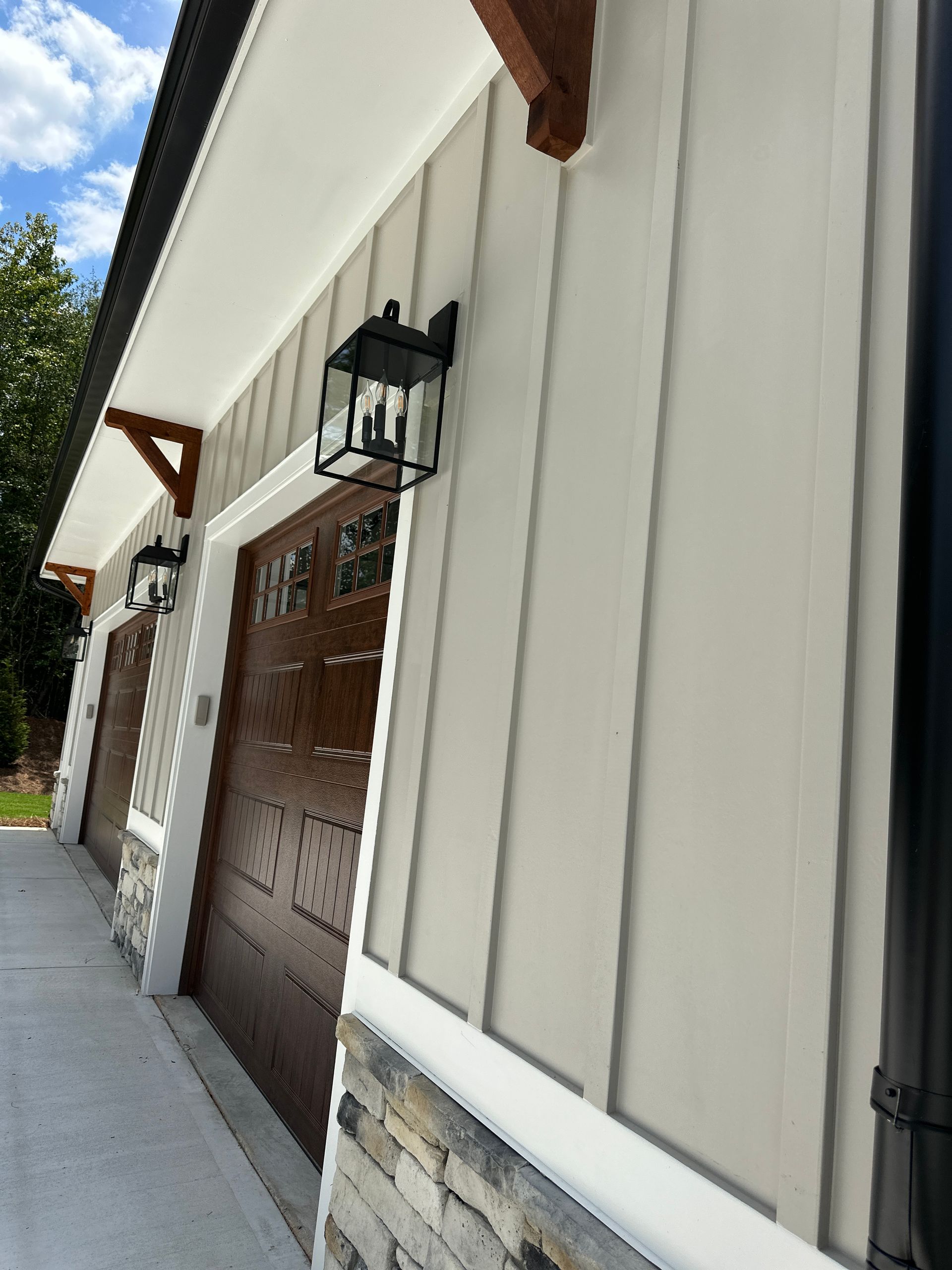 Exterior view of a garage with white siding, stone base, and brown wooden doors under a bright sky
