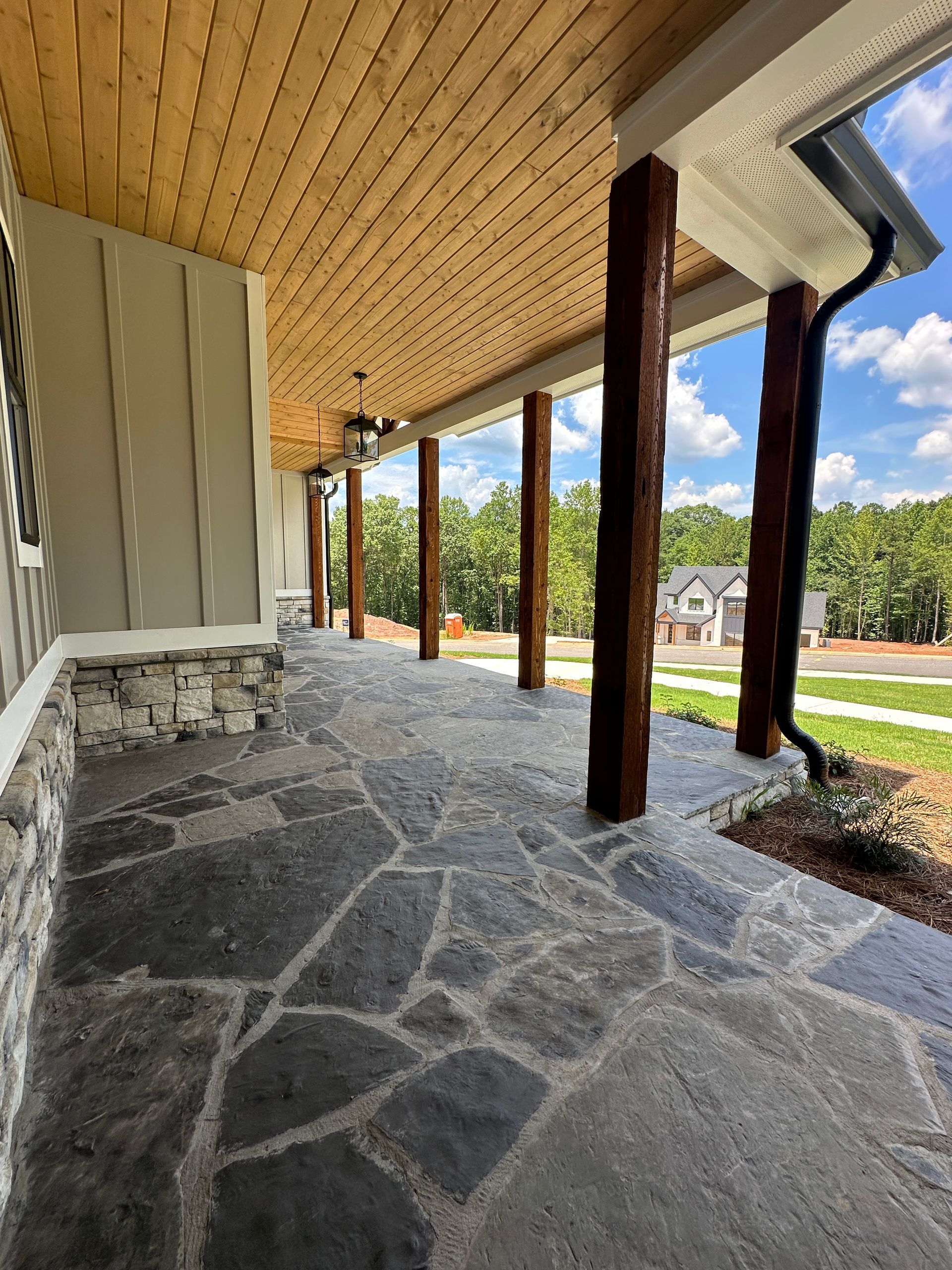 Stone porch with wood ceiling, dark columns, and a view of a grassy yard and houses beyond