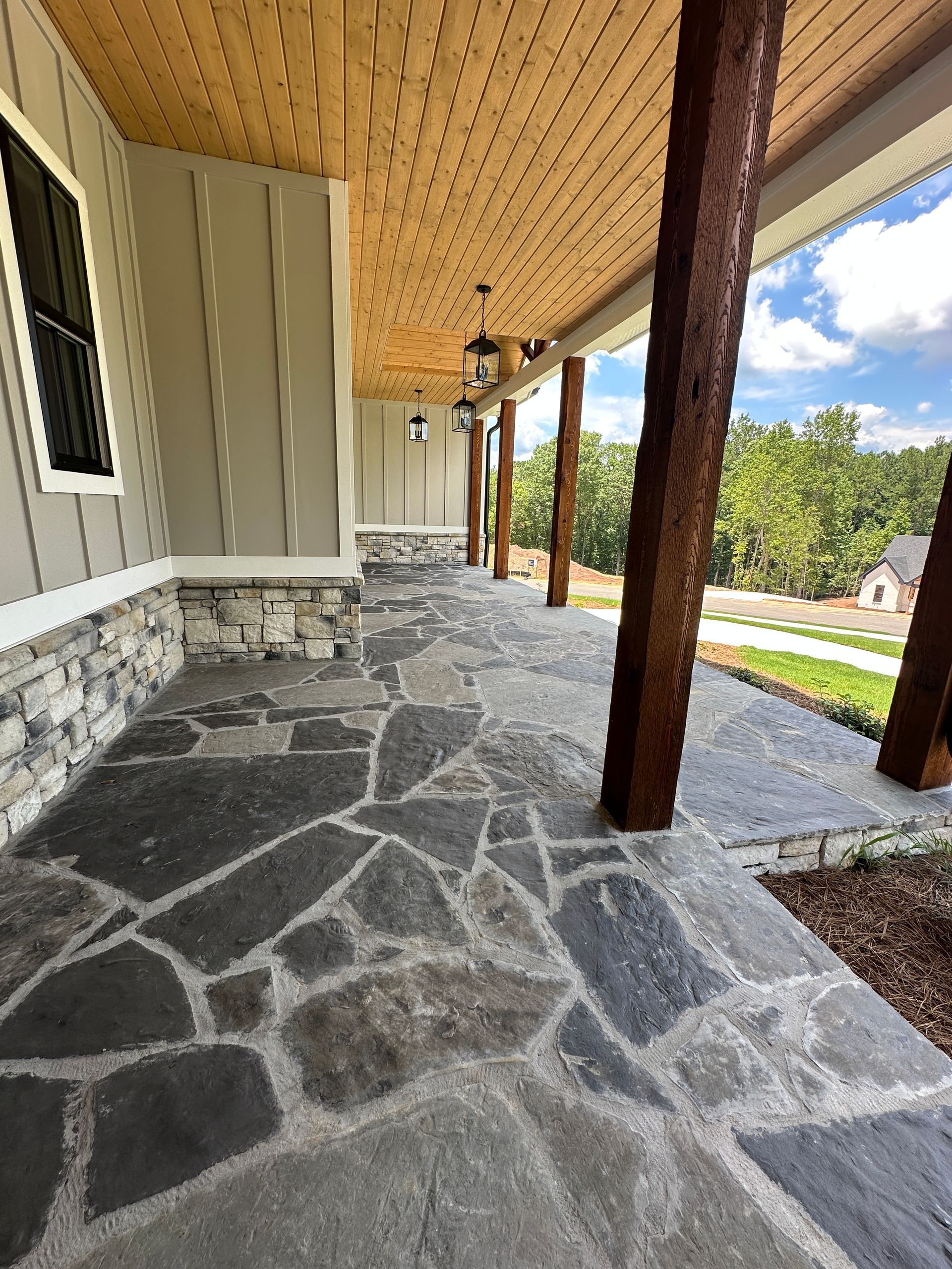 Stone porch with wooden posts, gray siding, and a view of the yard under a covered roof