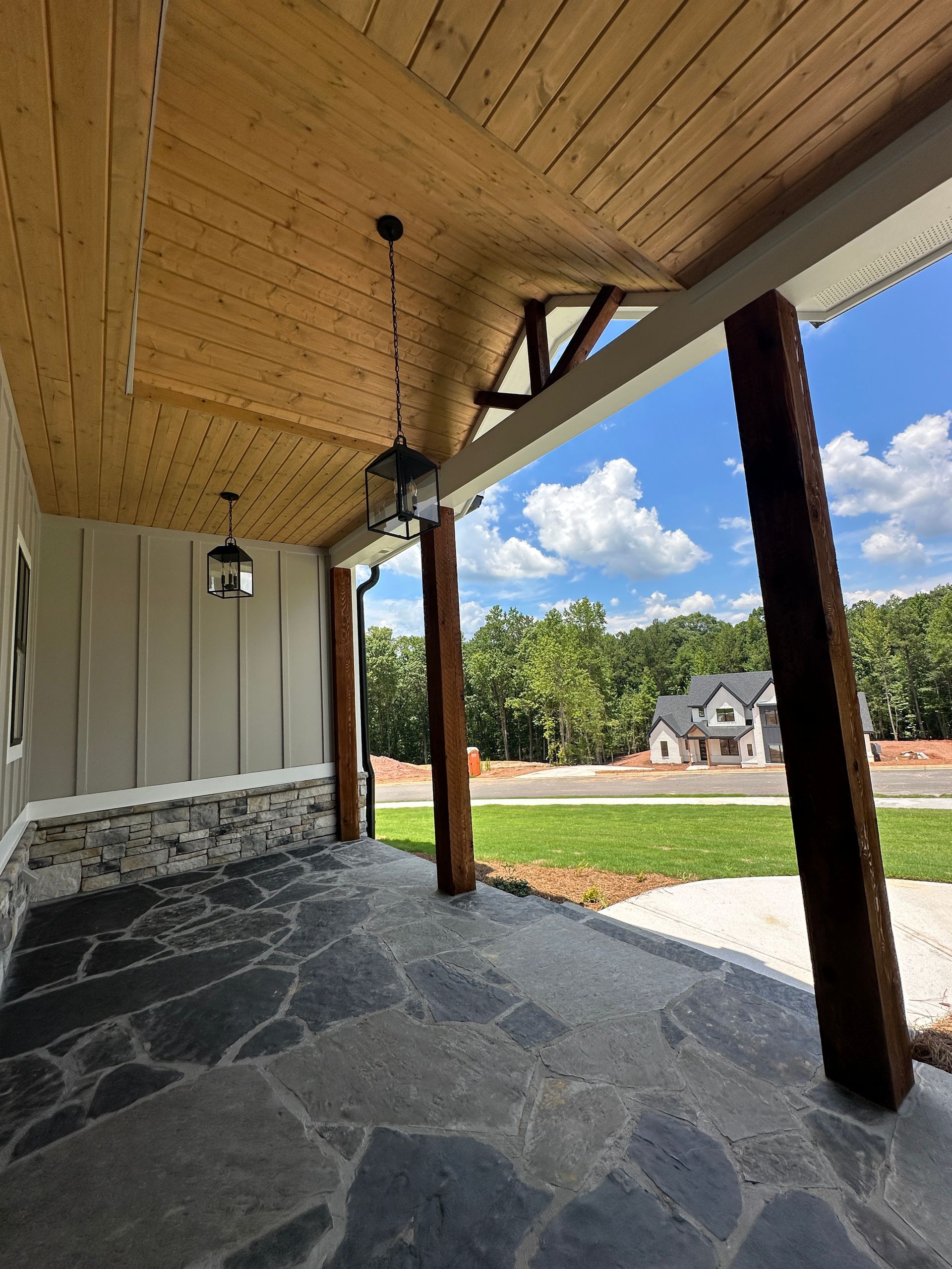 Covered front porch with stone floor, wood ceiling, and a view of a suburban street and house.
