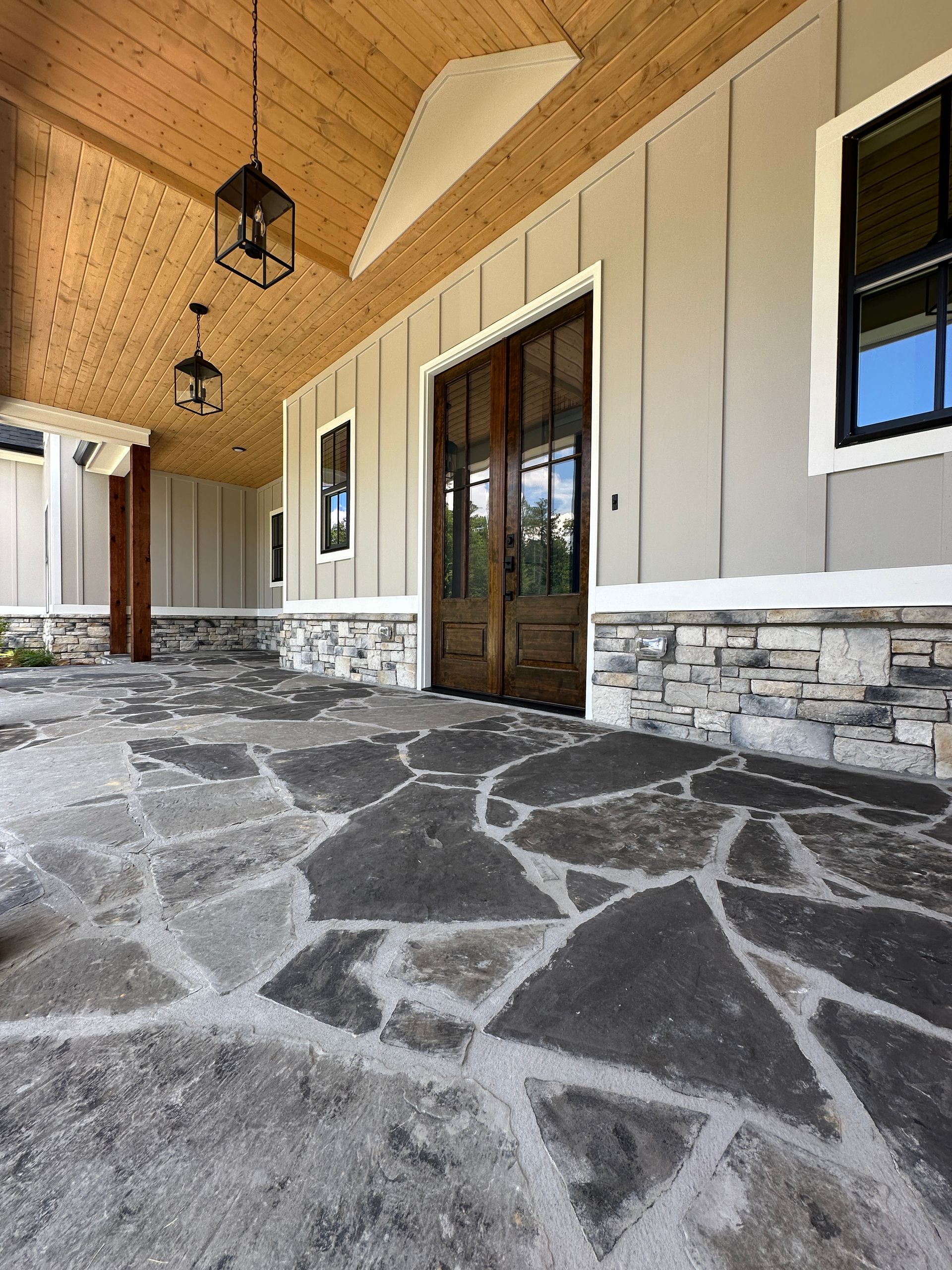 Covered stone porch with wood ceiling, hanging lanterns, and double glass doors on a house exterior
